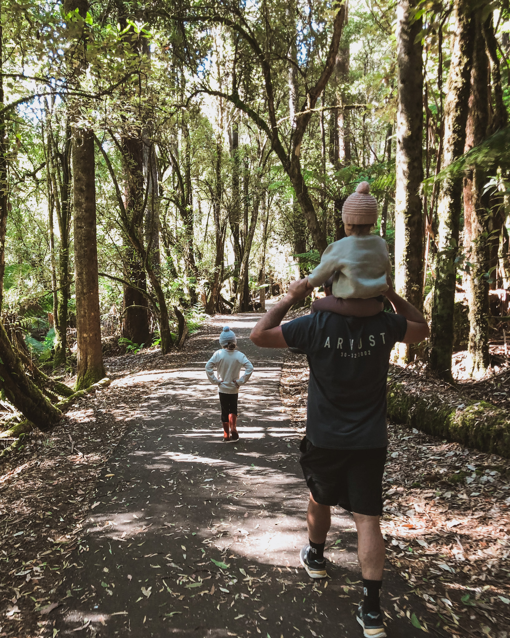 Young daughter sitting on her father's shoulders with her older sister leading the way during a forest hike, showcasing the value of staying active and healthy together, fostering a sense of adventure and well-being during travel.