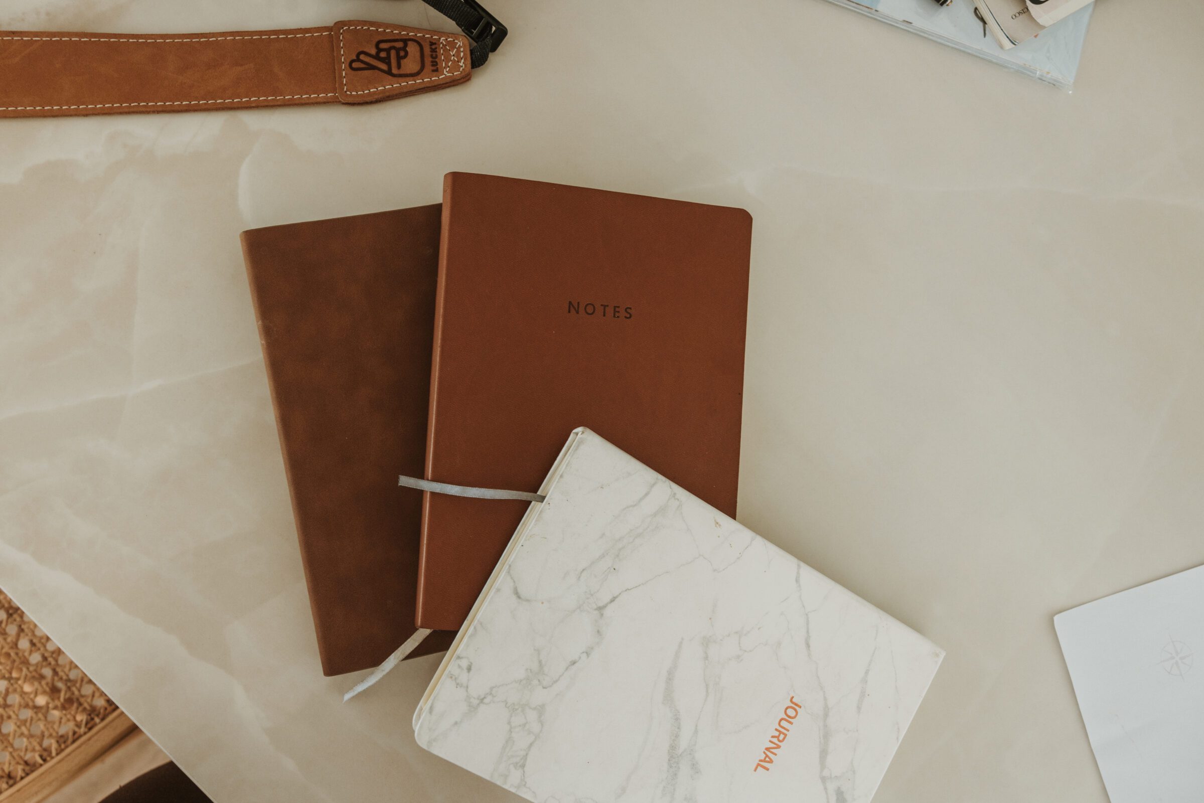 Camera strap, notebook, and journal laid out on a desk, symbolizing the detailed research and planning required in how to plan for a family vacation.