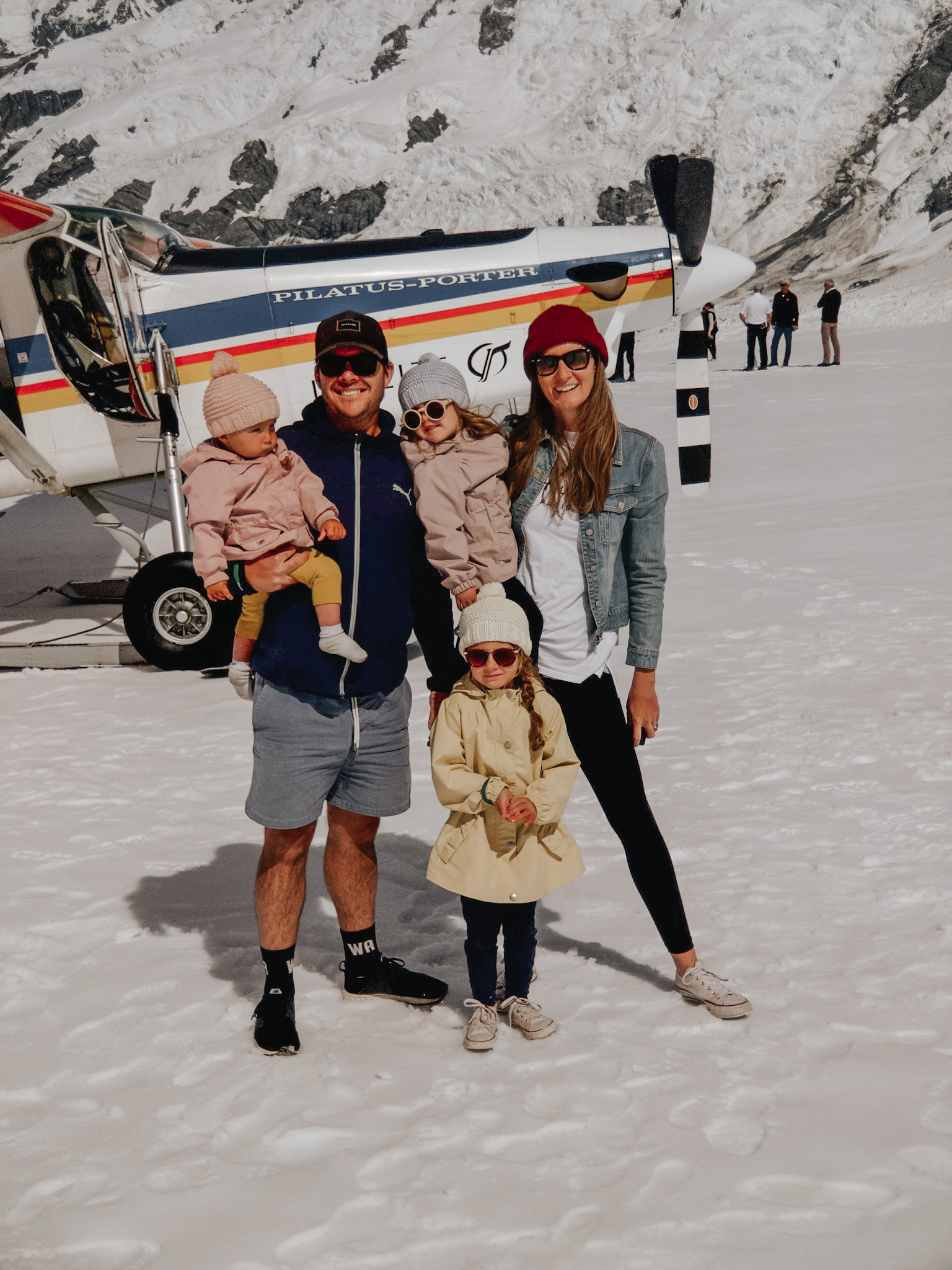 Family with three young children standing atop a glacier in New Zealand, reveling in the snow with a snow plane behind them, epitomizing high-low travel by merging the unique luxury experiences that can be included in a high-low travel strategy.