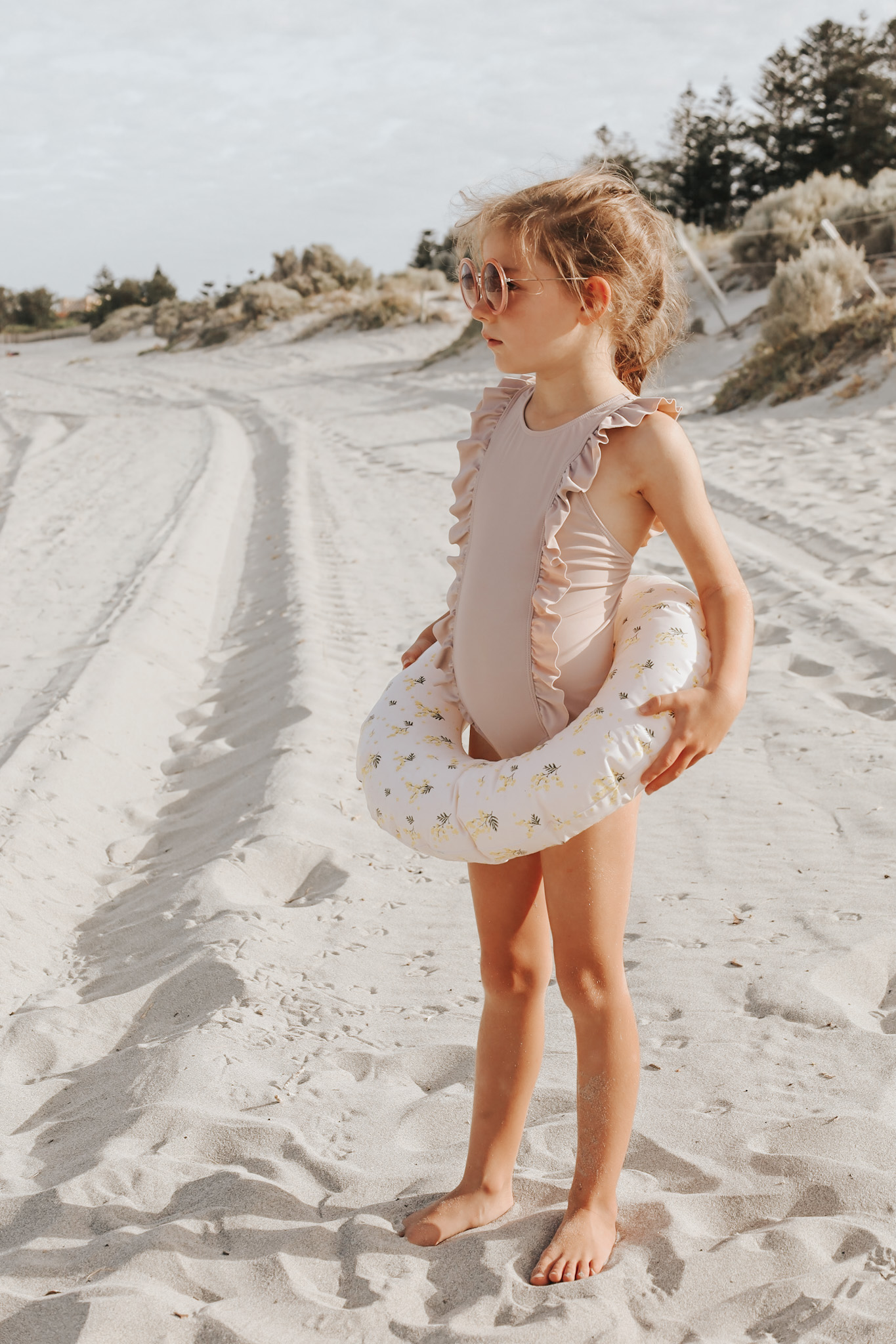 Young girl at the beach in pink bathers and sunglasses, holding a flotation ring, captures the essence of deciding where to take a family vacation, showcasing destinations that spark joy and excitement in children as a key factor in the decision-making process.