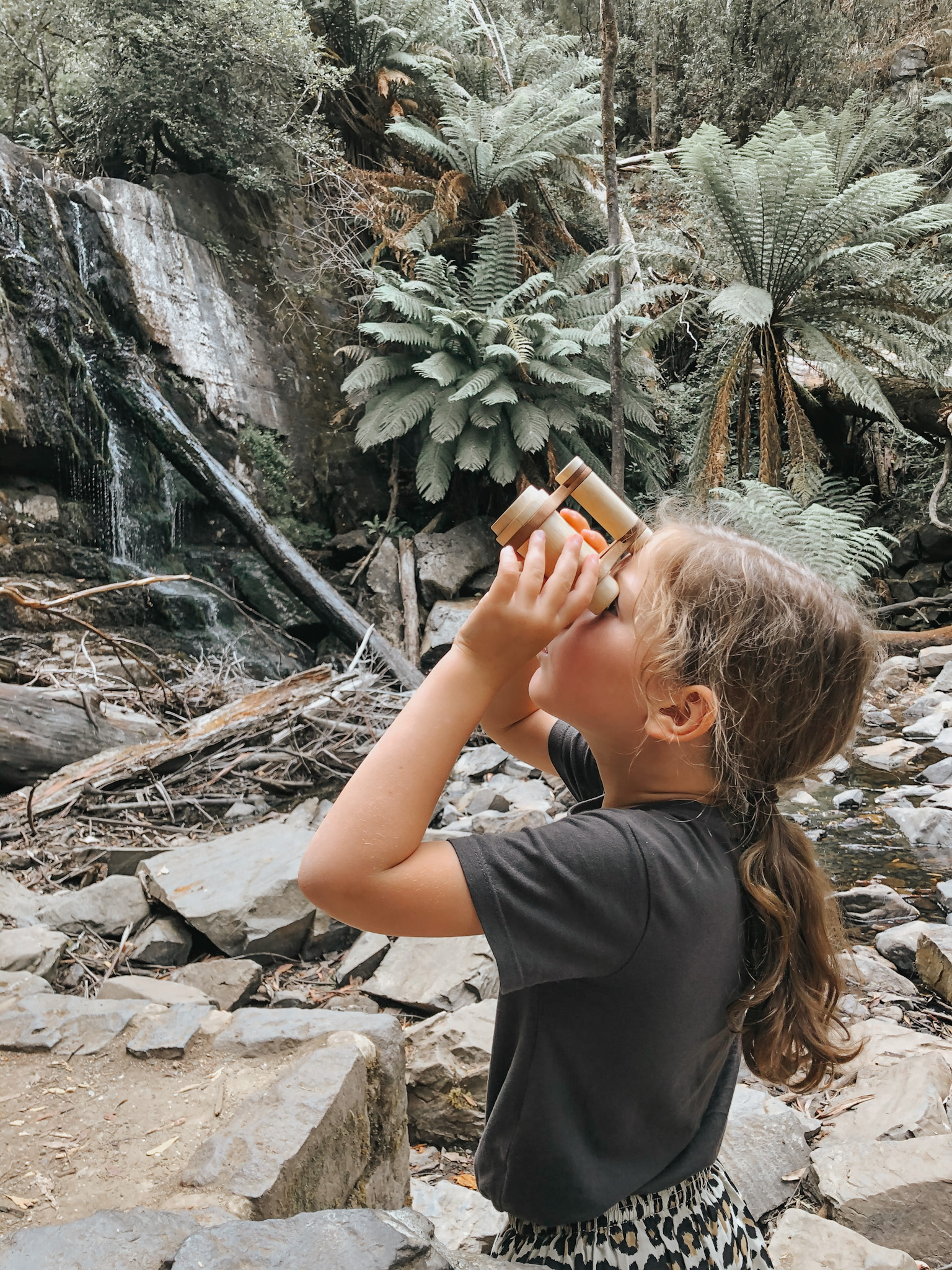 Young girl in nature using toy binoculars to look up and explore her surroundings, capturing the spirit of adventure and curiosity in choosing a family vacation destination that encourages exploration and discovery.