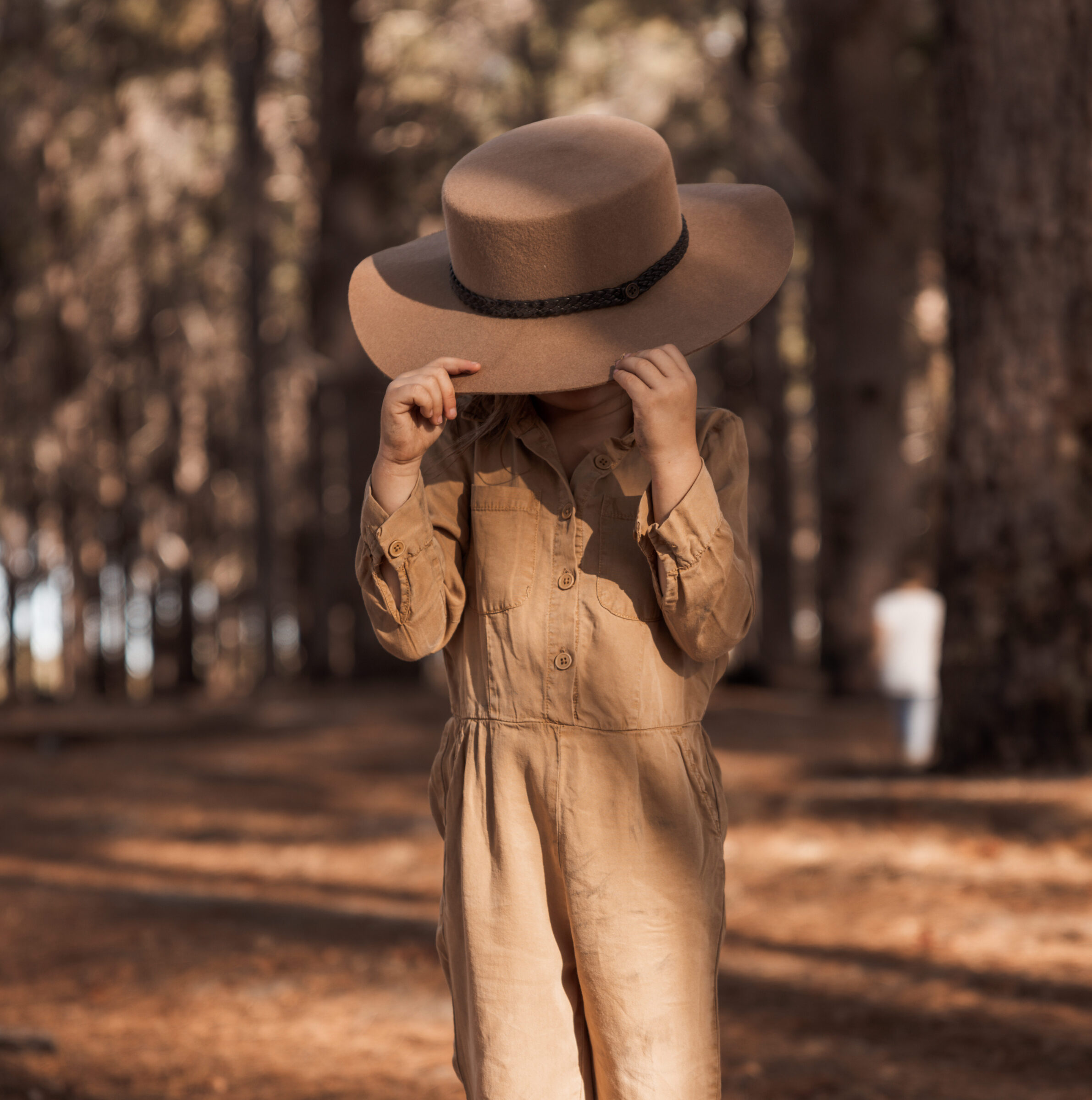 5-year-old girl in the woods wearing her mother's oversized hat, playfully hiding her face, symbolizing that travel doesn't have to stop once you have kids.