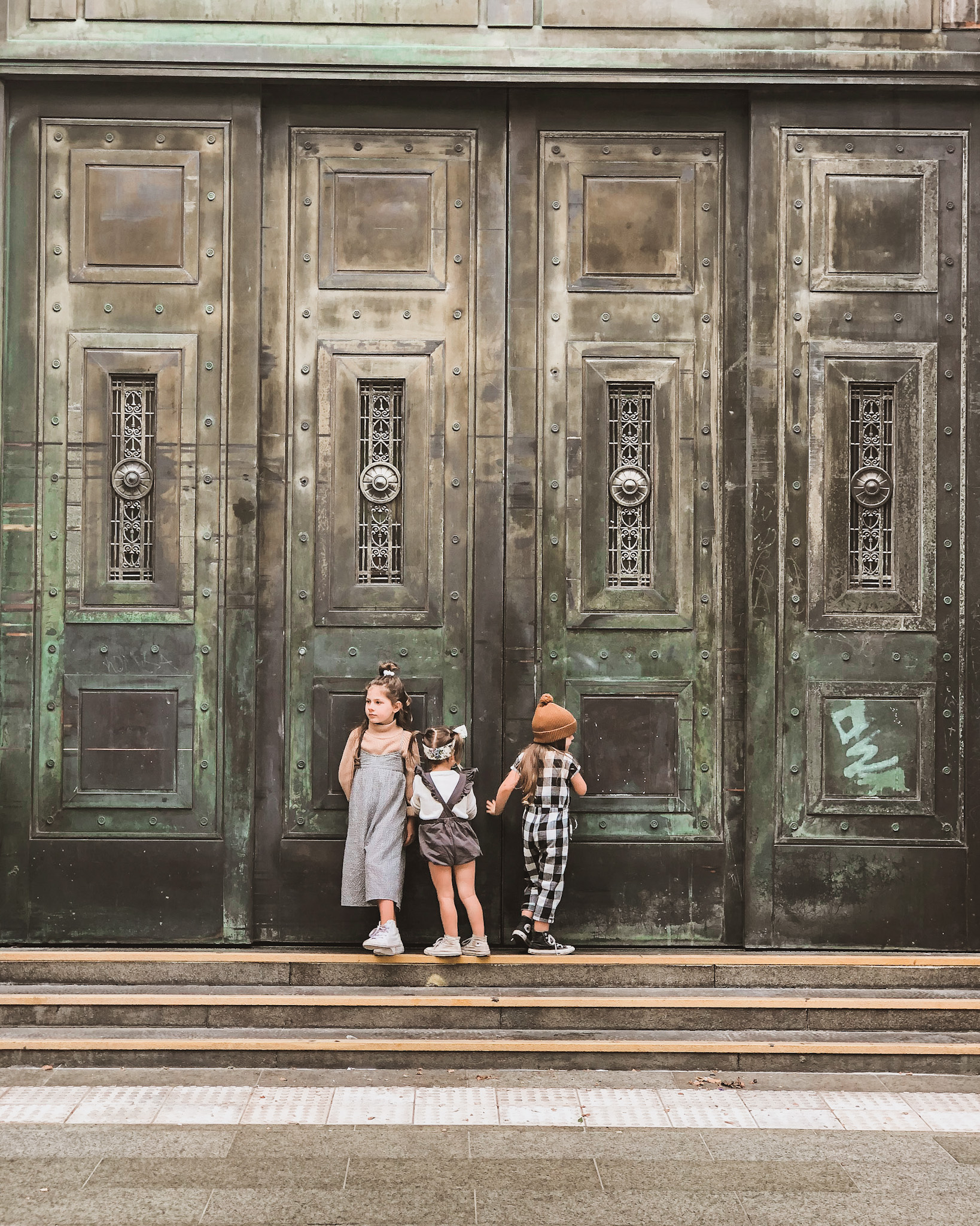 Three young sisters exploring a local city, standing in front of elaborate doors, showcasing how to plan for a family vacation that encourages children's curiosity and discovery.