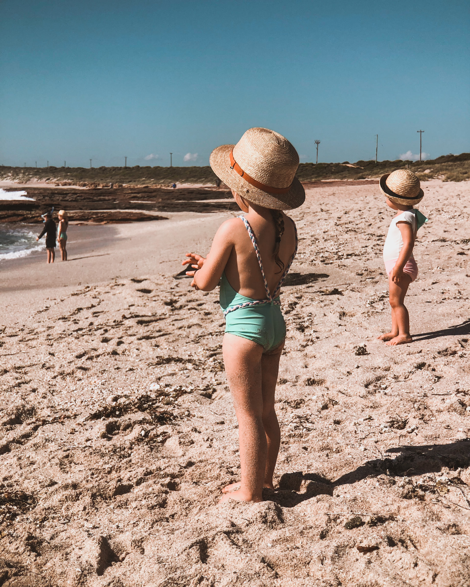 Does travel have to stop once you have kids? Four young children standing on the beach looking out to the ocean, illustrating how beach holidays can be part of a high-low travel strategy. The free activity of enjoying the beach allows families to allocate more budget towards luxurious accommodation or dining out, showcasing a smart way to afford travel by prioritizing what matters most to the family.