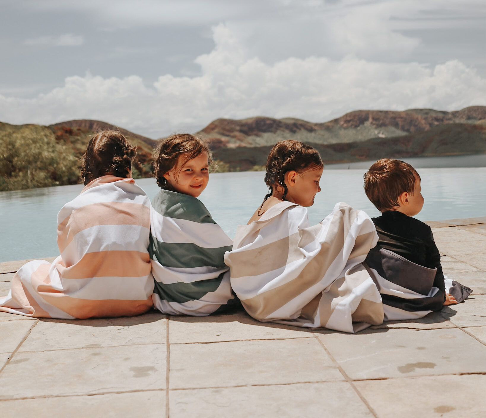 Four children wrapped in towels, sitting by an infinity pool overlooking the breathtaking Kimberley landscape, embodying the joy of a well-planned family vacation.