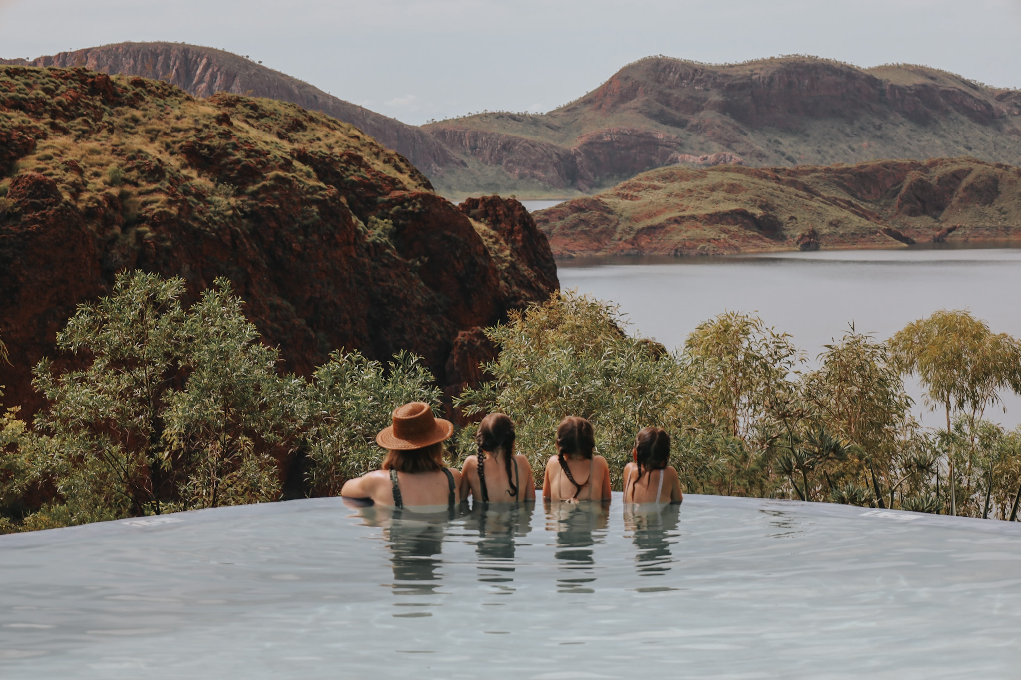 Mother and her three daughters leaning on a pool wall, looking out to the Australian Kimberley scenery during the wet season, capturing the essence of finding a family vacation destination during low season for better flight deals, demonstrating how to decide where to take a family vacation based on both beauty and budget considerations.