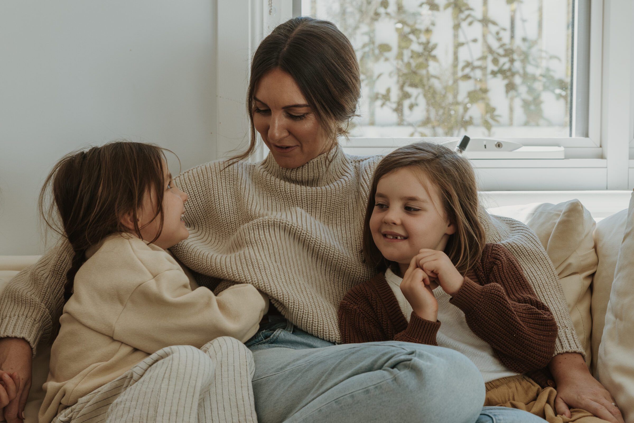 Mother cuddling with her two young daughters on a couch, enjoying precious moments together, embodying the significance of slowing down to cherish time together when planning for a family vacation, highlighting the value of these moments in the overall vacation experience.