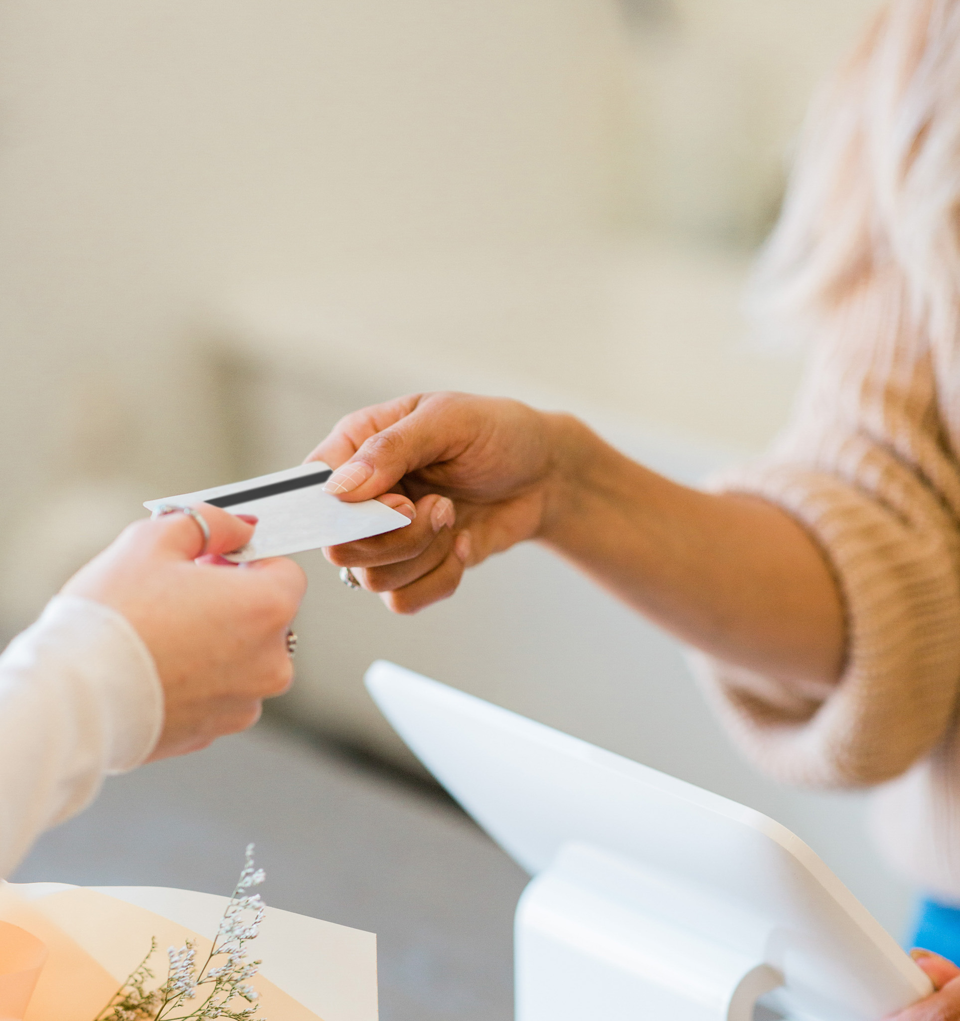 Close-up of hands exchanging a bank card at a shop counter, with a sales computer visible, illustrating practical aspects of managing money while travelling overseas.