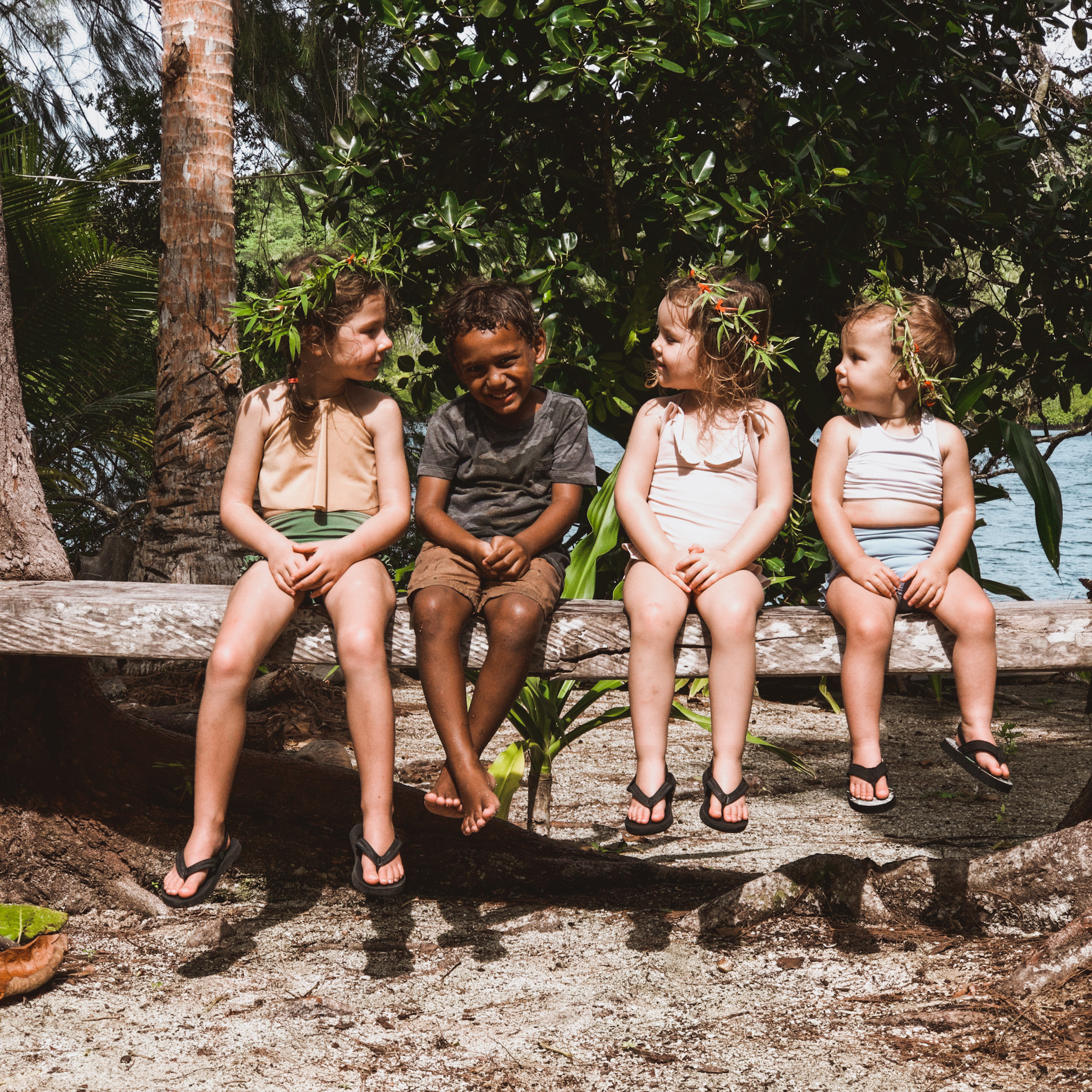 Three young sisters sitting on a tree log with a young local boy in the Solomon Islands, highlighting the new friendships and cultural exchanges that enrich the travel experience for children.