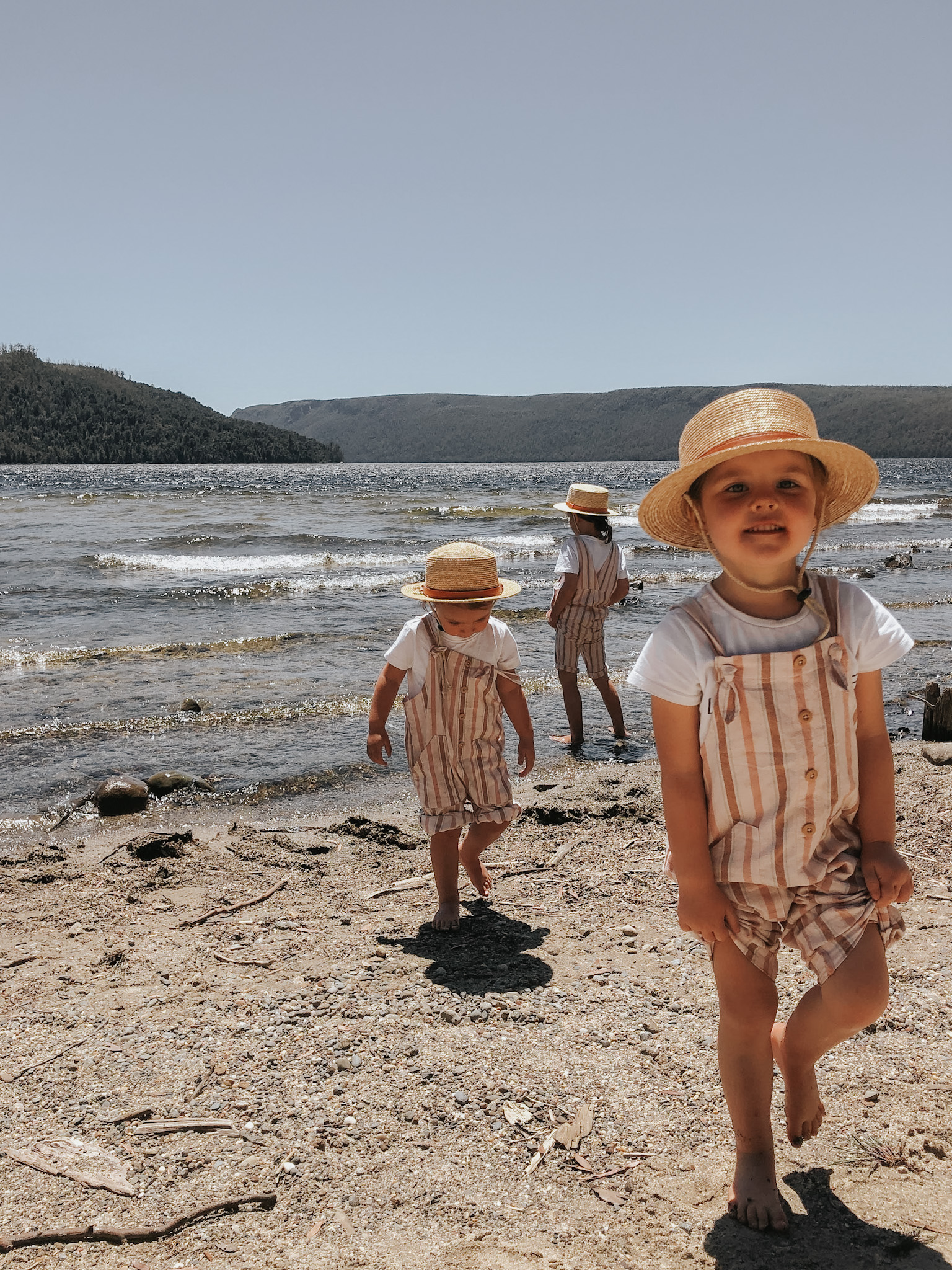 Three young sisters playing on the sand of a lake in Tasmania, capturing a moment of joy and exploration, highlighting the family-oriented decision-making process on where to vacation, emphasizing destinations that offer enriching experiences for children.