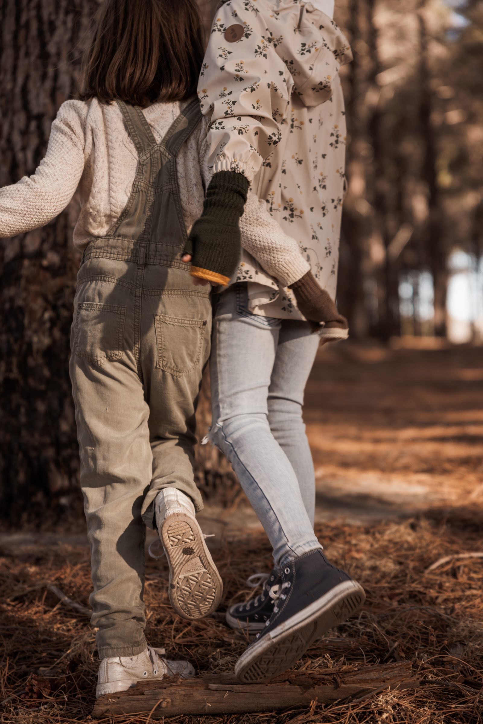 Two young sisters with their arms around each other, walking and exploring a forest together, embodying the importance of a family vacation by showcasing the bond and adventure that comes with discovering new surroundings as a family.