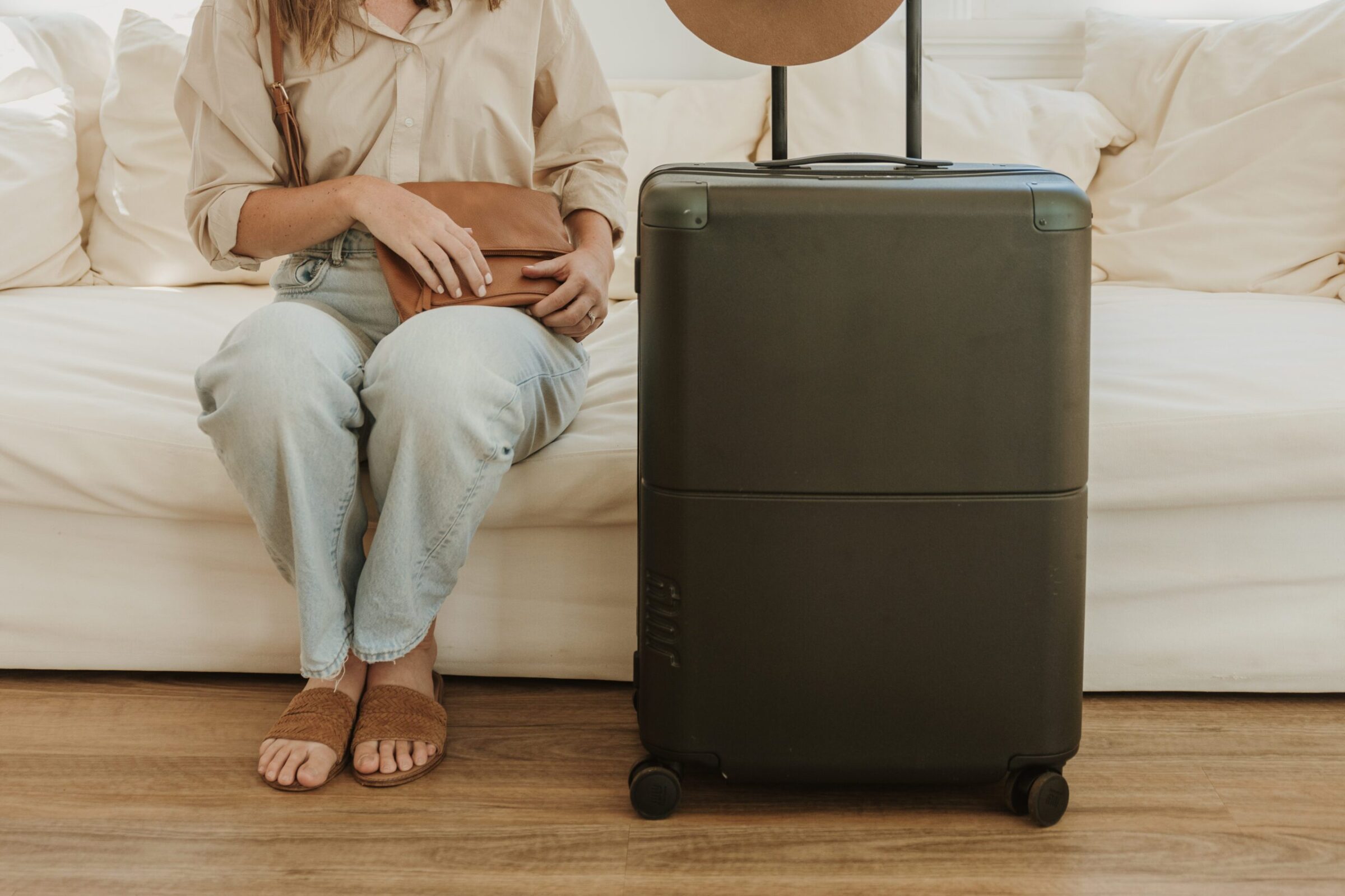 Woman sitting on a couch next to her suitcase, preparing to open her purse, symbolizing the best way to bring money on a trip overseas.