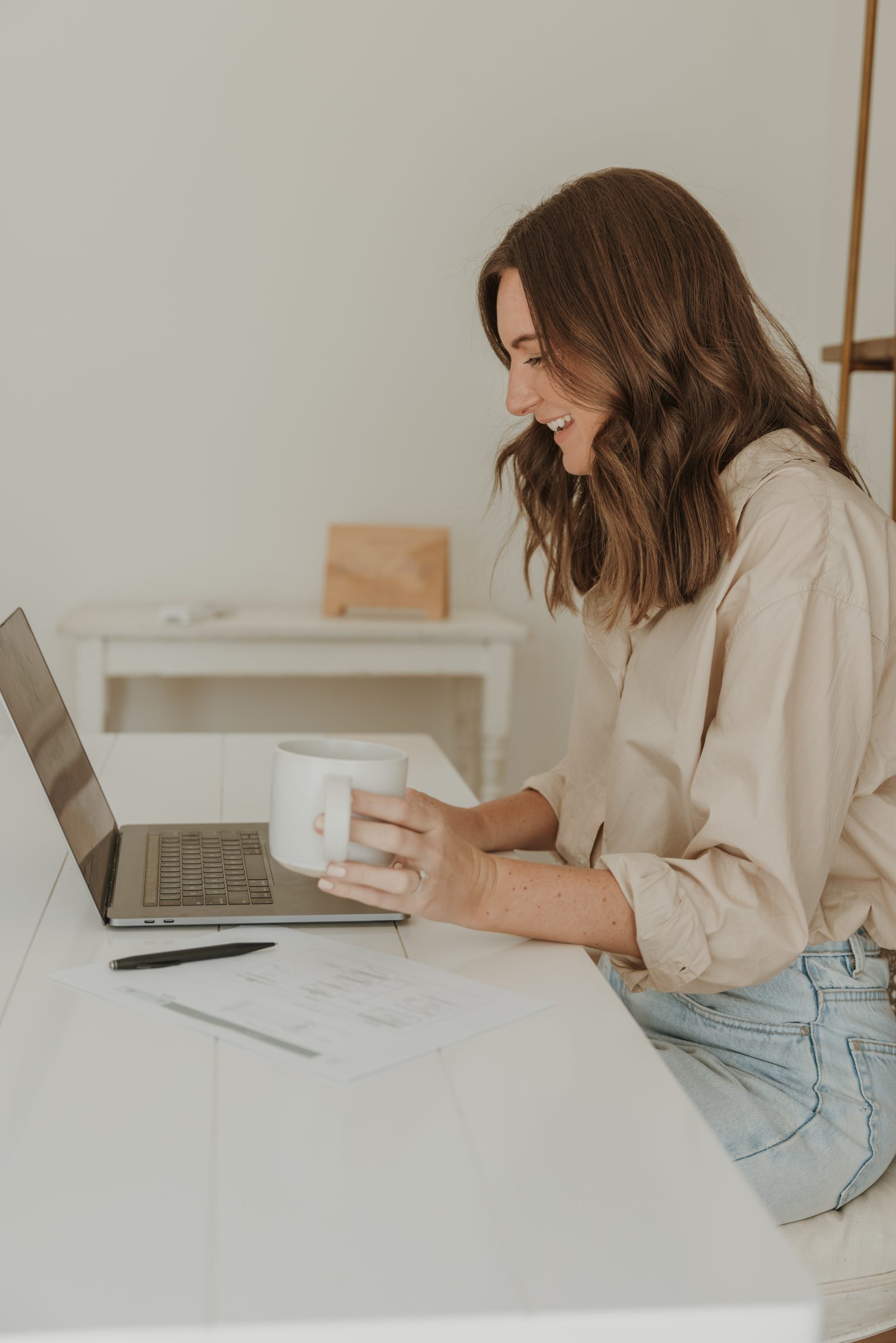 Mother at her desk with coffee, typing on her laptop to organize her family travel budget, embodying how to plan for a family vacation by clarifying financial categories to ensure sufficient savings and avoid surprises during the trip.