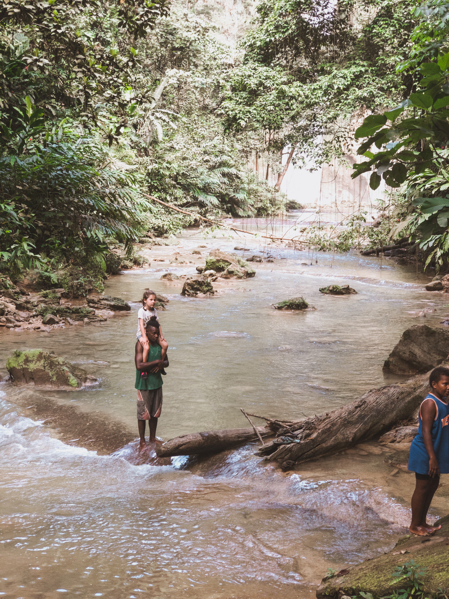 Young girl sitting on the shoulders of a local Solomon Island man, finishing a family jungle hike, illustrating the importance of a family vacation through the lens of cross-cultural communication and support, as she learns to navigate and appreciate diverse environments and people.