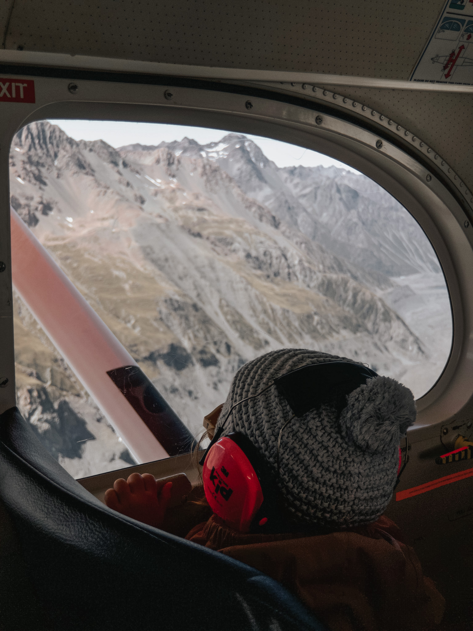 Young girl gazing out the window of a snow plane en route to a glacier in New Zealand, taking advantage of age-based discounts, as she enjoys a free ticket for being under 6, offering families affordable ways to explore together.