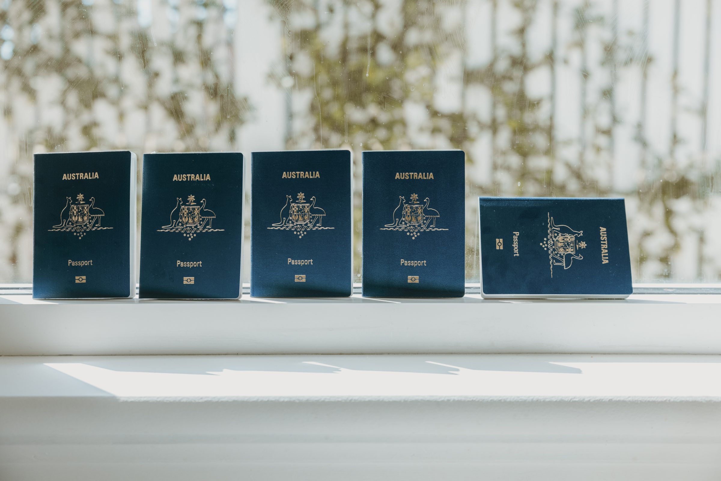 Five family passports sitting on a window sill, ready for an upcoming holiday, highlighting the grown-up yet crucial aspect of 'how do you pack for travel with kids'—organizing travel documents. Emphasizes that, while focusing on children, their documents are equally important for smooth travel experiences.