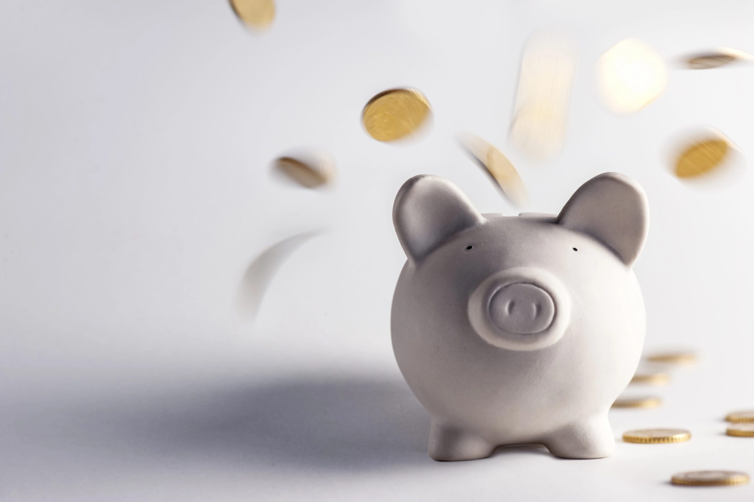 White piggy bank with gold coins being poured over it, symbolizing the importance of including a buffer in your family travel budget for unexpected expenses. This image highlights the need for financial preparedness to ensure a smooth and stress-free family vacation.