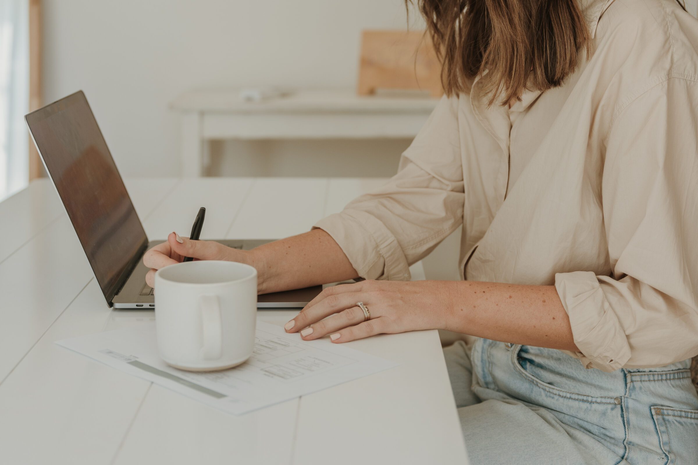 Woman at her desk working on a laptop with a printed spreadsheet and pen, meticulously planning daily expenses like transport and meals for an upcoming holiday. This scene captures the essence of 'how to create a family travel budget,' emphasizing detailed preparation to manage travel costs effectively.