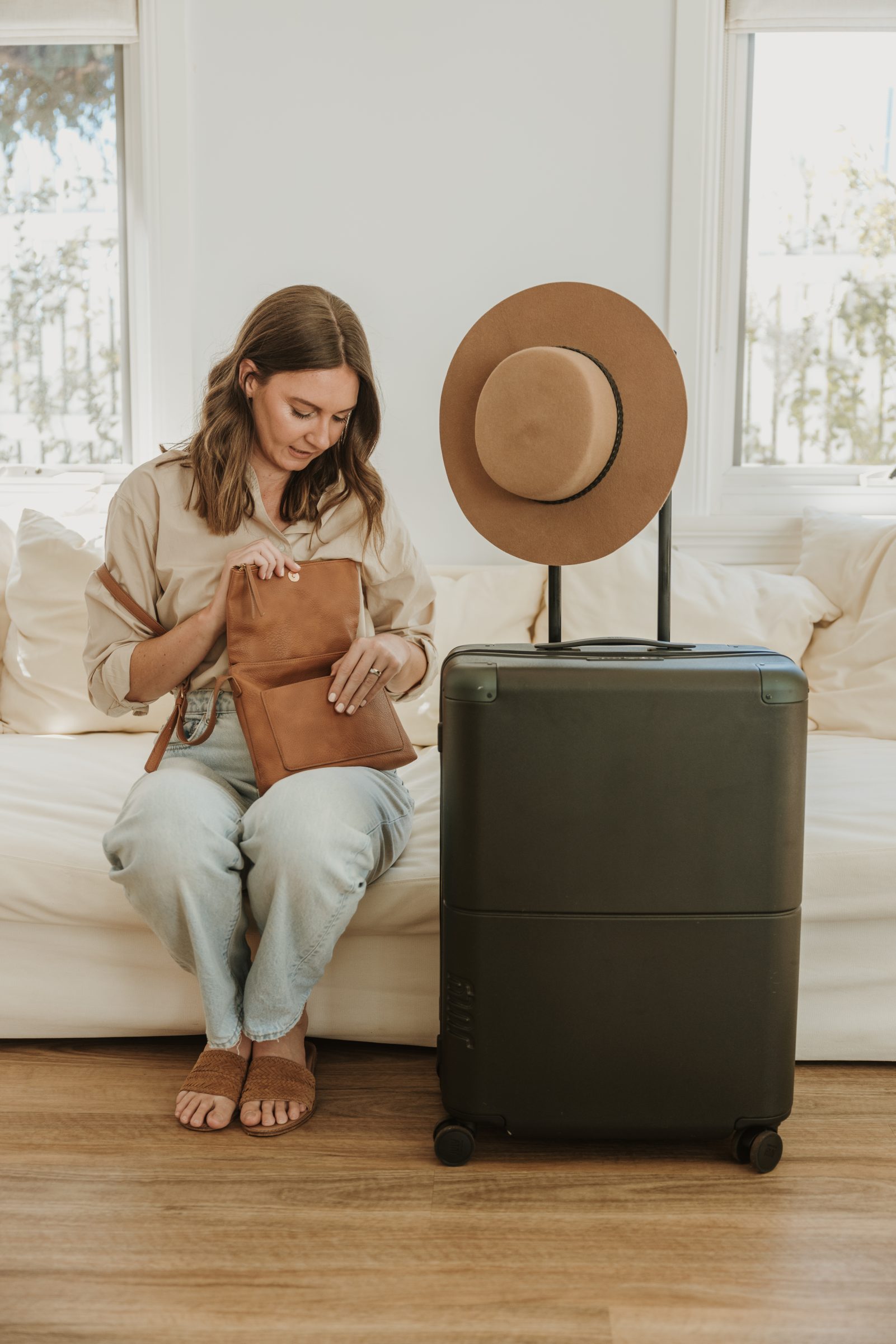 Woman sitting on her couch beside her suitcase, checking her handbag to ensure she has the correct financial setup for her trip, demonstrating 'how to create a family travel budget' by preparing financially to handle expenses effectively while traveling.