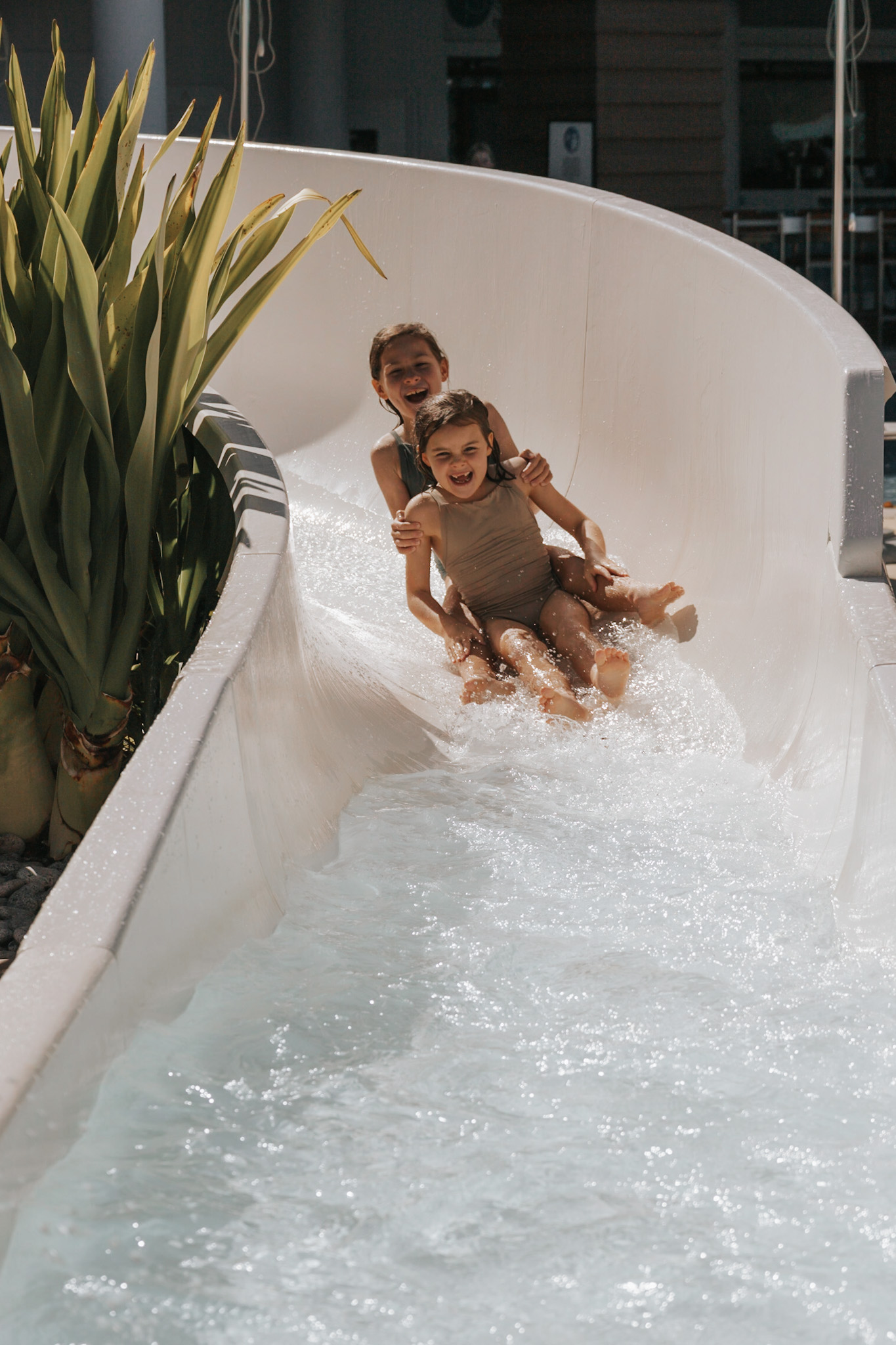 Two young sisters laughing and smiling as they come down a water slide, embodying the joy of prioritizing spending on activities that matter most during a family vacation. This image exemplifies how to afford your next family vacation by illustrating strategic budget allocation—choosing to save on accommodations if daytime activities like theme parks are the highlight, ensuring families enjoy what they love most without overspending.