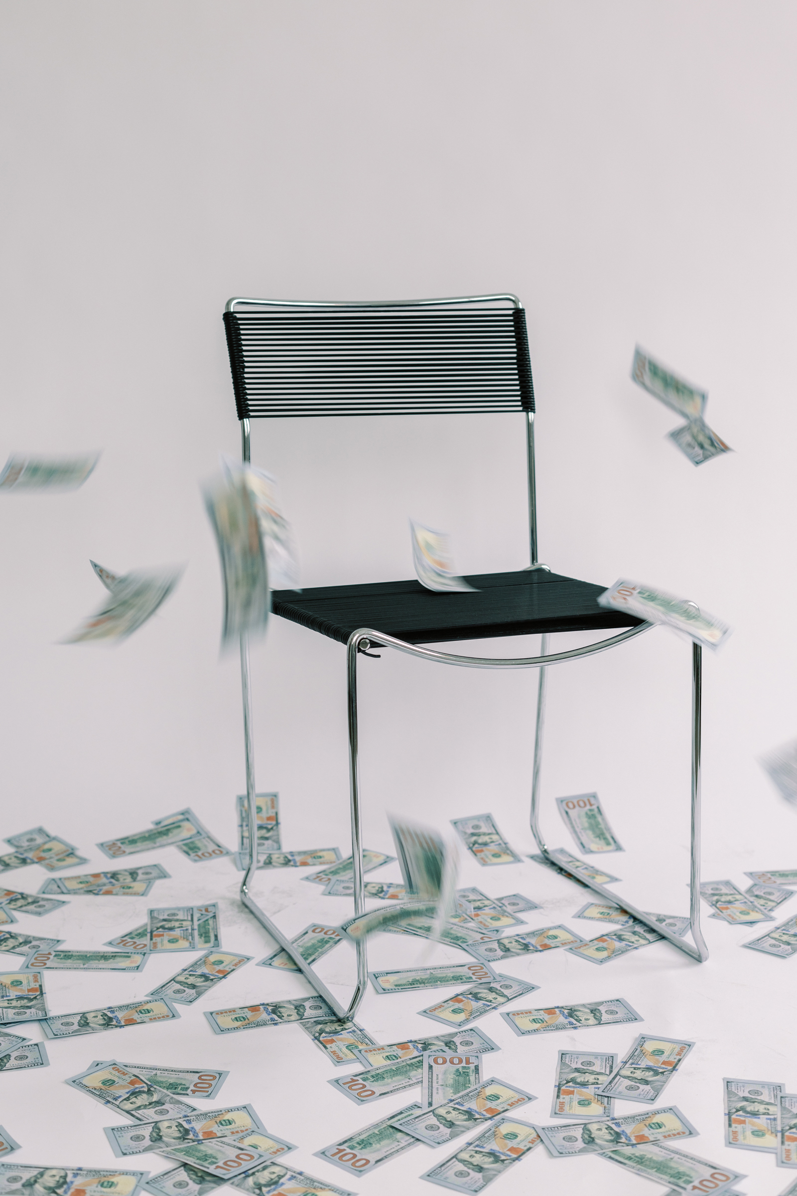 Chair in the middle of a room with a white background, with cash floating down around it, illustrating the strategy of using cash instead of cards to control spending. This image encourages adopting cash for daily expenses to physically feel the money being spent, making one more conscious of purchases and potentially saving more for travel by avoiding unnecessary spending.