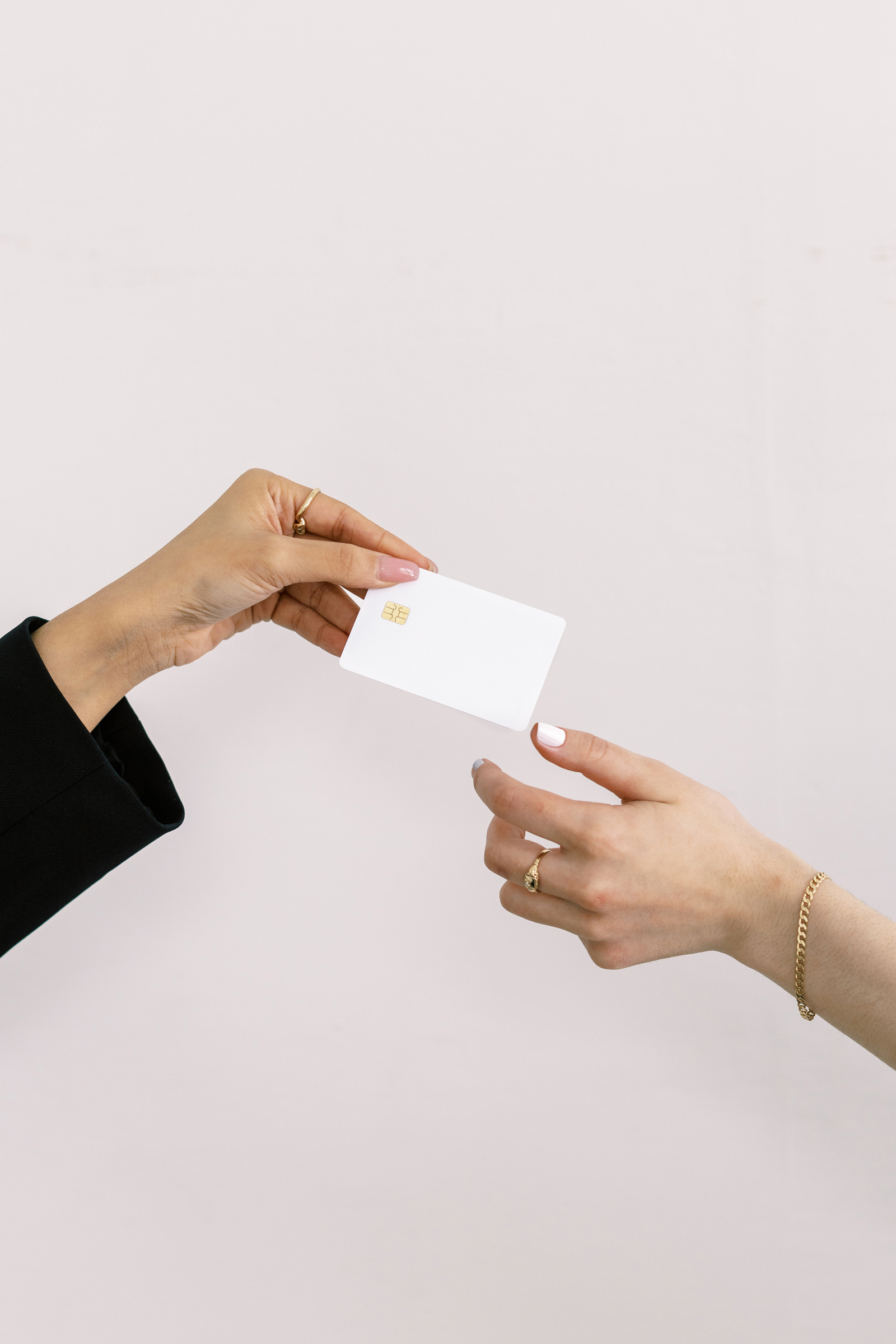 Woman's hand passing a bank card to another woman's hand, symbolizing the discipline involved in managing impulse buys through the 'wait two days' rule, a creative way to save money for travel by encouraging thoughtful spending.