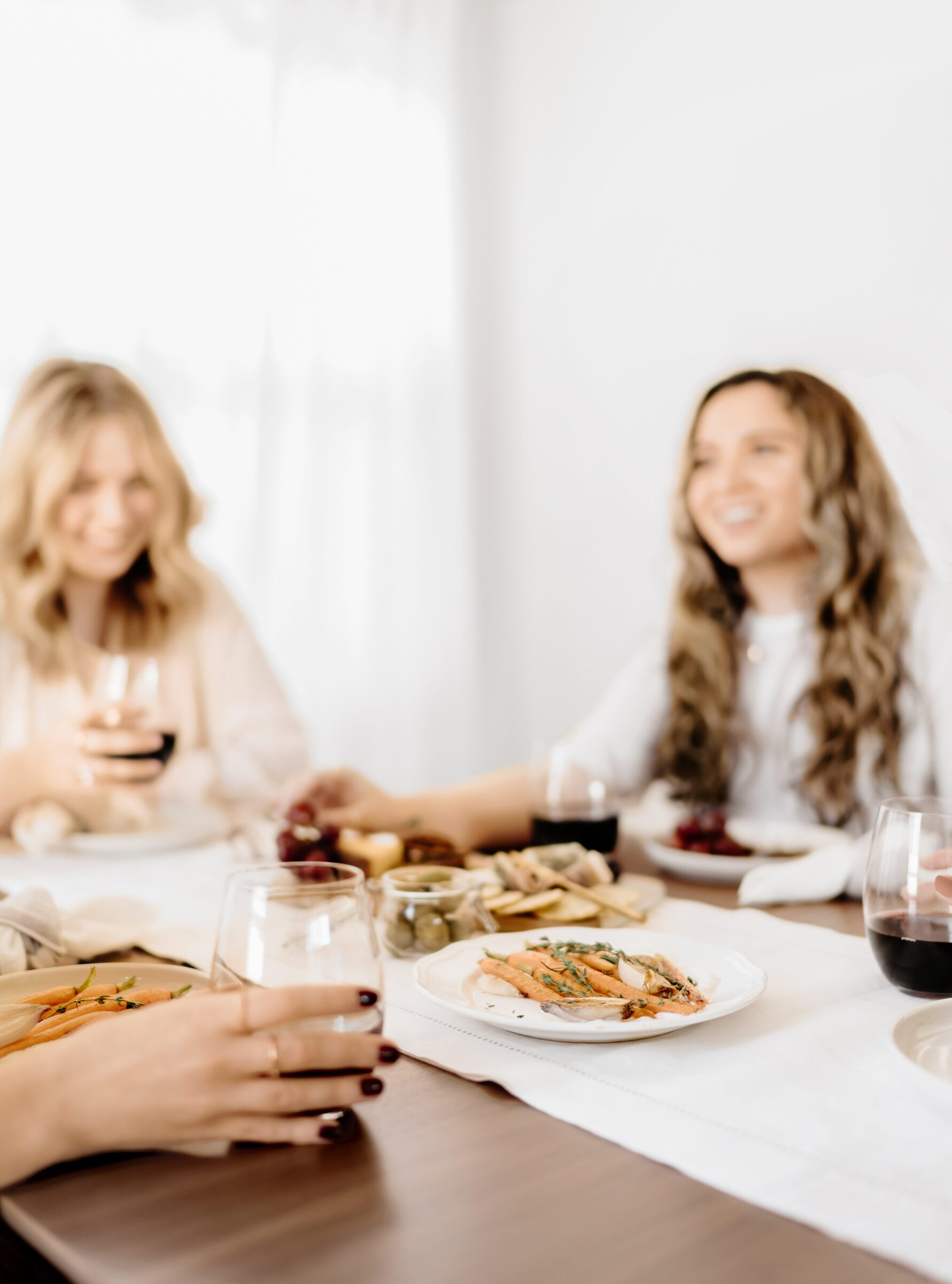 Group of women enjoying a meal together at home, symbolizing creative ways to save money for travel by opting to cook at home instead of dining out. This image highlights the financial benefits and social enjoyment of hosting friends for a potluck or simple gathering, allowing savings from avoided restaurant costs to contribute directly to a travel fund.