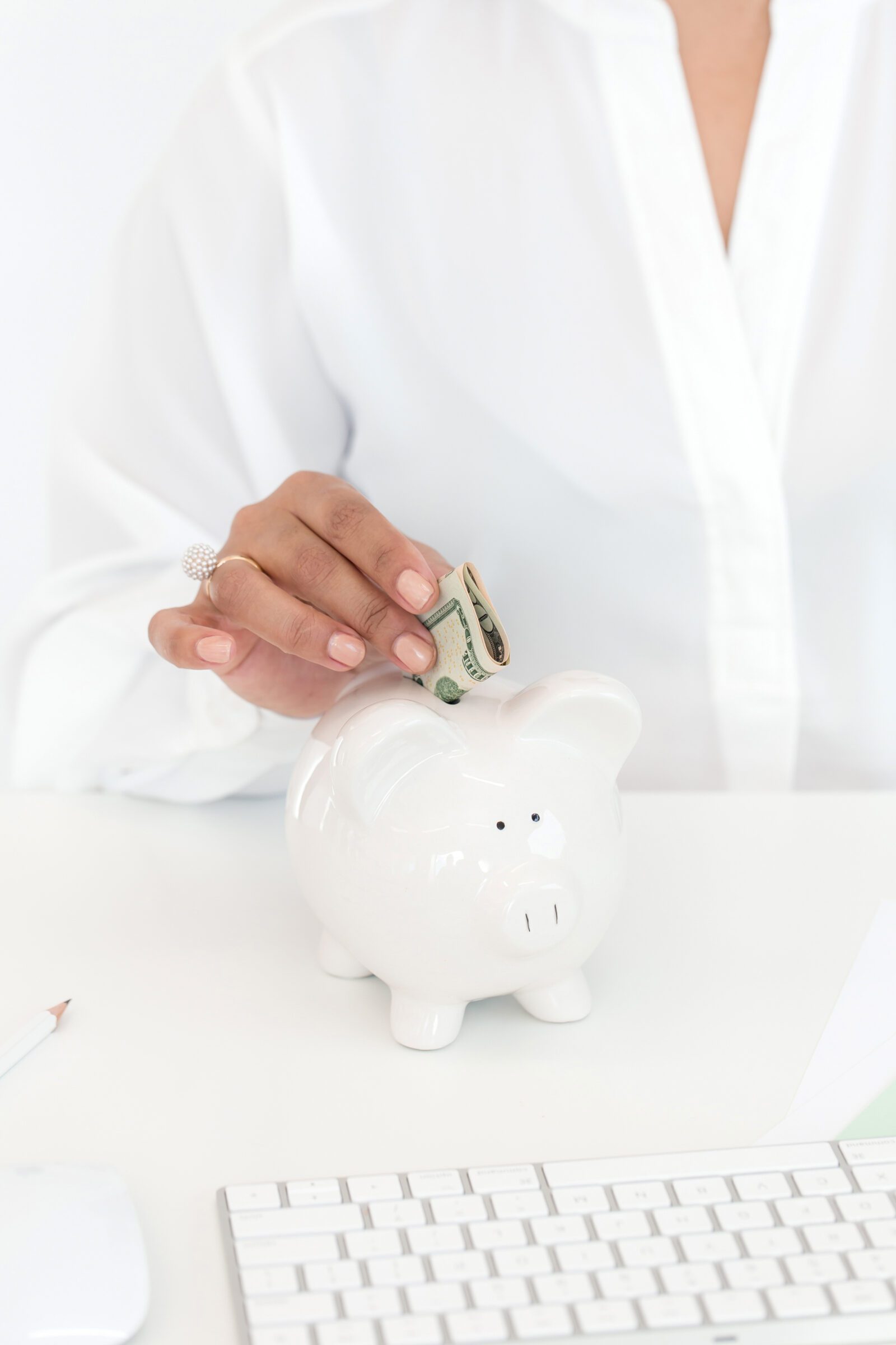 Woman in a white blouse depositing folded cash notes into a white piggy bank, illustrating a proactive approach to saving for travel by regularly contributing to a travel fund.