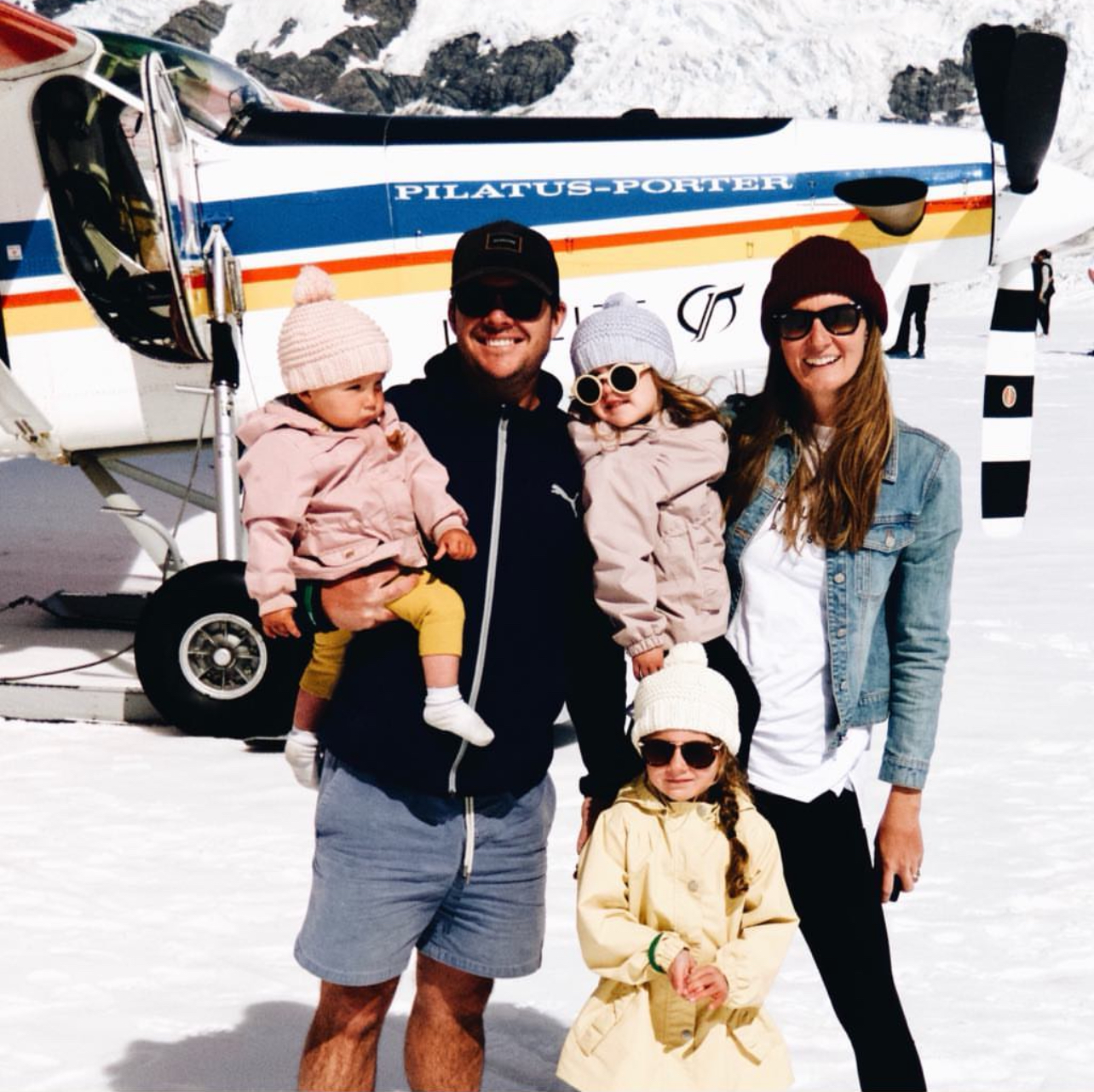 Parents with three young children under five years old standing on a glacier in New Zealand in front of the snow plane they flew in on, illustrating the financial benefits of traveling with young kids. This image highlights how families can save through age-related discounts like free flights for toddlers and reduced rates for young children, significantly lowering the overall cost of unique experiences like helicopter tours.