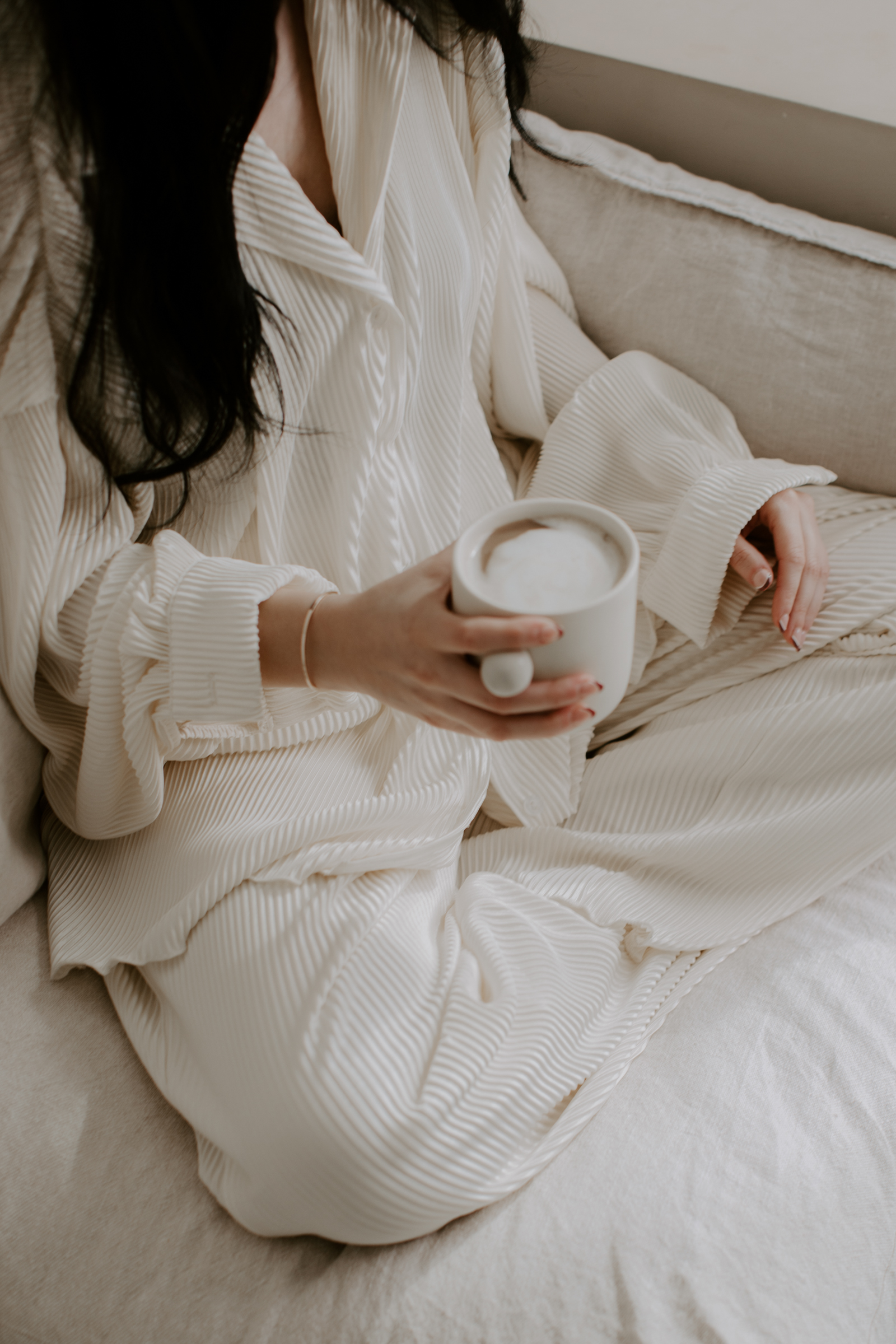 Woman sitting on her couch at home, holding a coffee, exemplifying creative ways to save money for travel by rethinking costly habits. This image highlights the balance of enjoying life's pleasures, like a coffee at home, while cutting back on daily expenses to boost the travel fund.