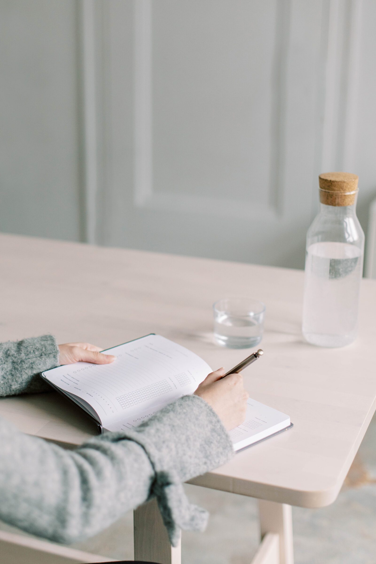 Woman at table with notebook and pen, sipping water, emphasizing the importance of setting specific savings goals for travel. Detailed planning, including costs for flights, accommodation, and activities, transforms abstract desires into tangible targets, driving focused saving efforts. 