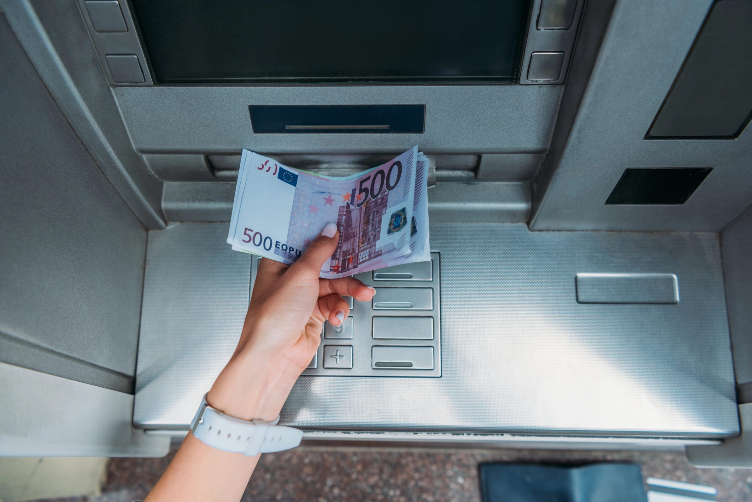 Top view of a woman withdrawing cash from an ATM, illustrating the importance of secure banking, strong PINs, and safe money access while travelling overseas.