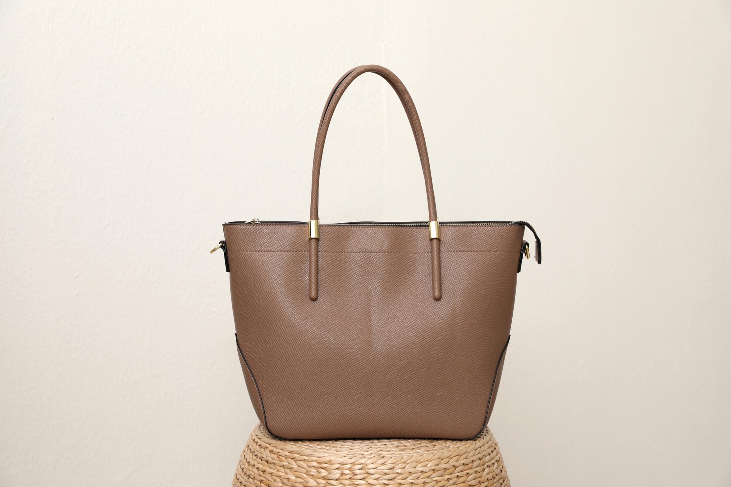Stylish woman's bag placed on a wicker stand near a light wall, representing items to prepare for a trip. Ideal visual for a financial travel checklist to organise belongings before going overseas.