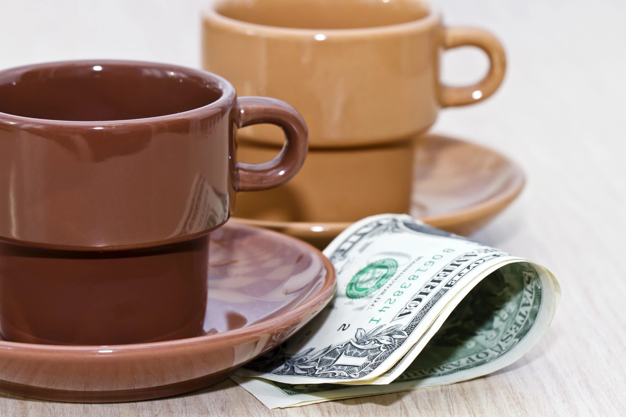 Cash notes placed under an empty coffee cup, highlighting the need to research local tipping customs as part of planning your travel money system overseas.