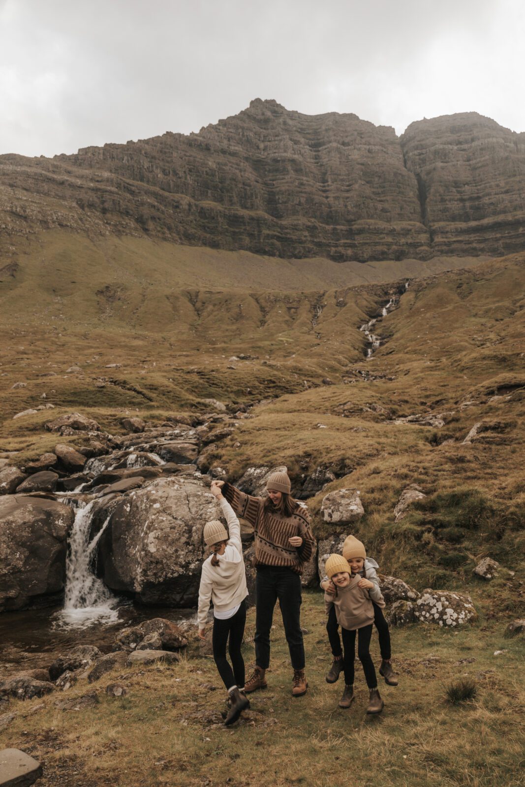 Our family standing in front of a waterfall and mountains in the Faroe Islands, illustrating the importance of setting specific travel goals to make trips real, motivating, and easier to grow your travel savings for.