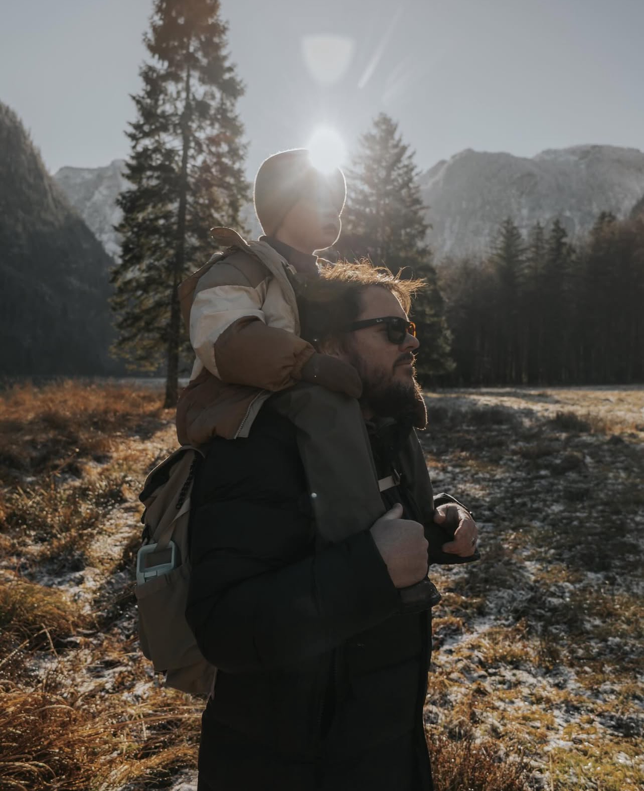 Young boy sitting on his dad’s shoulders in Germany at sunset with mountains behind them, illustrating quick wins for growing travel savings through creative challenges and cutting costs.