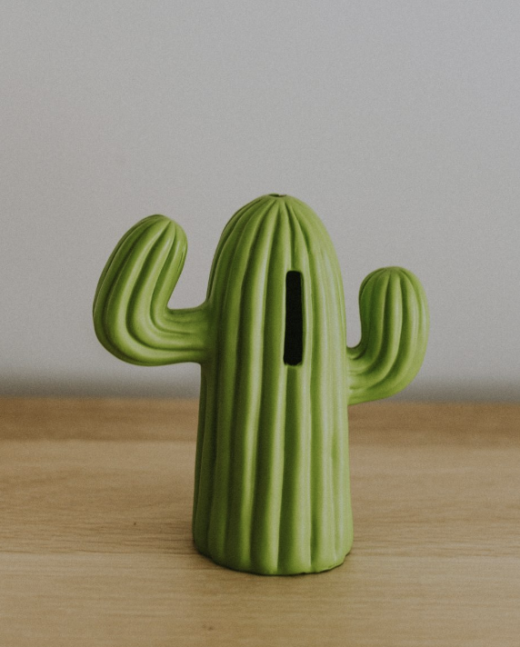 Cactus-shaped money bank sitting on a wooden table, representing creative ways to grow your travel savings and keep your travel savings thriving.