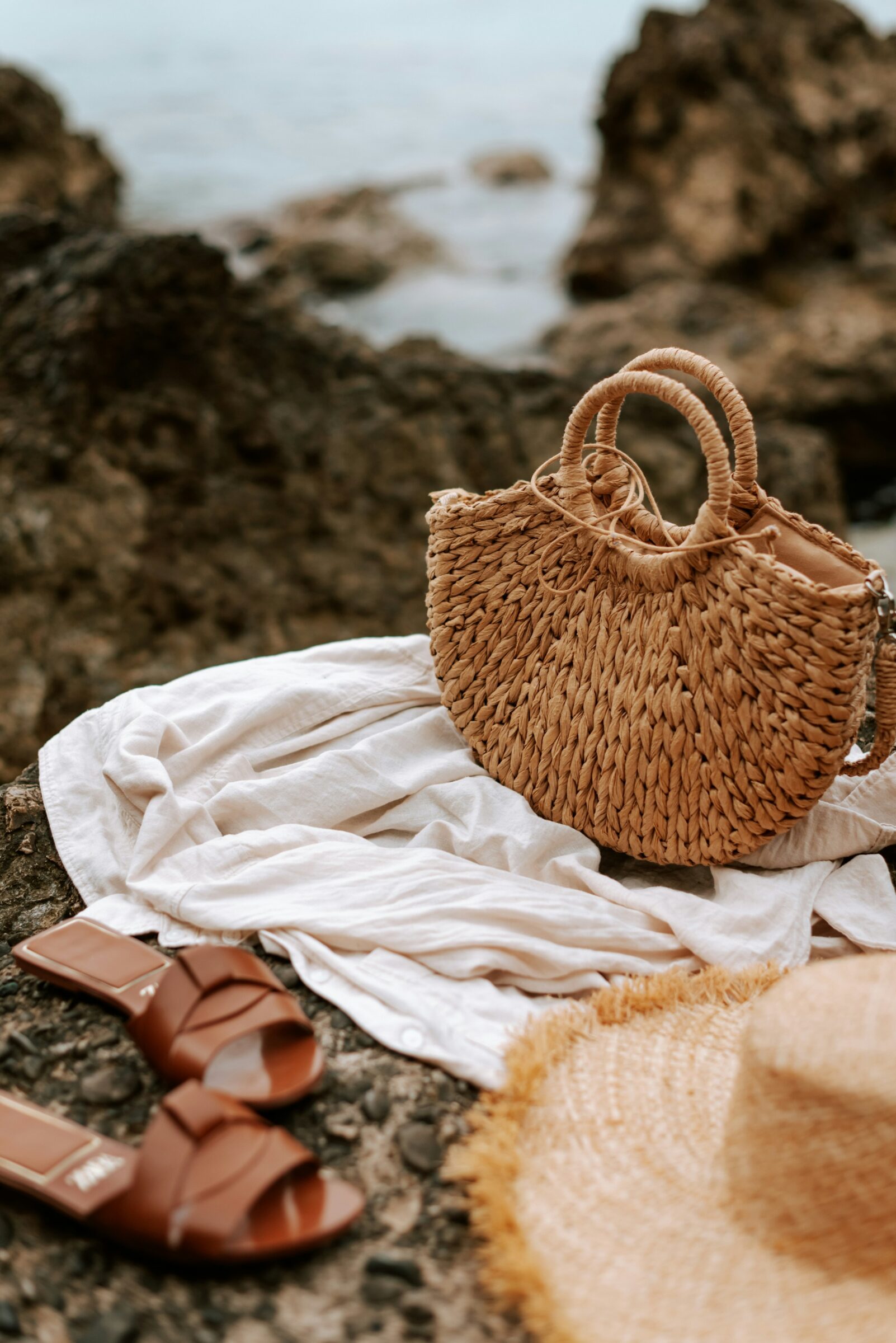 Straw beach bag, hat, and sandals placed on a towel by the sea, representing relaxed beach travel moments and the importance of keeping valuables secure while away from your belongings.