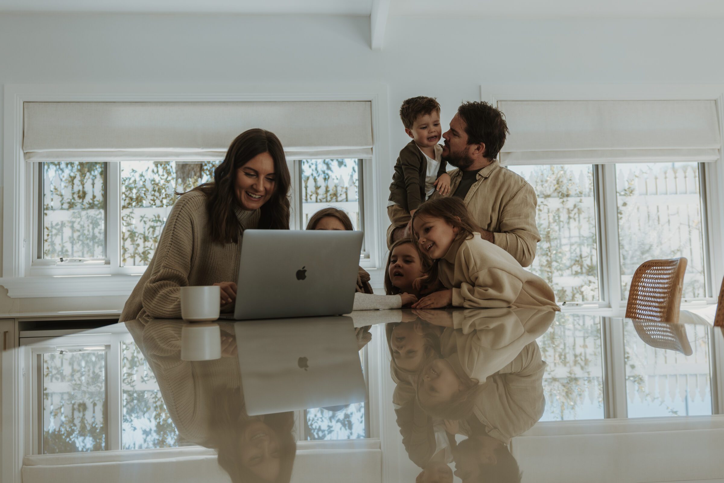 Parents and kids smiling around a kitchen bench, checking bank accounts on a laptop as part of keeping track of money while abroad.