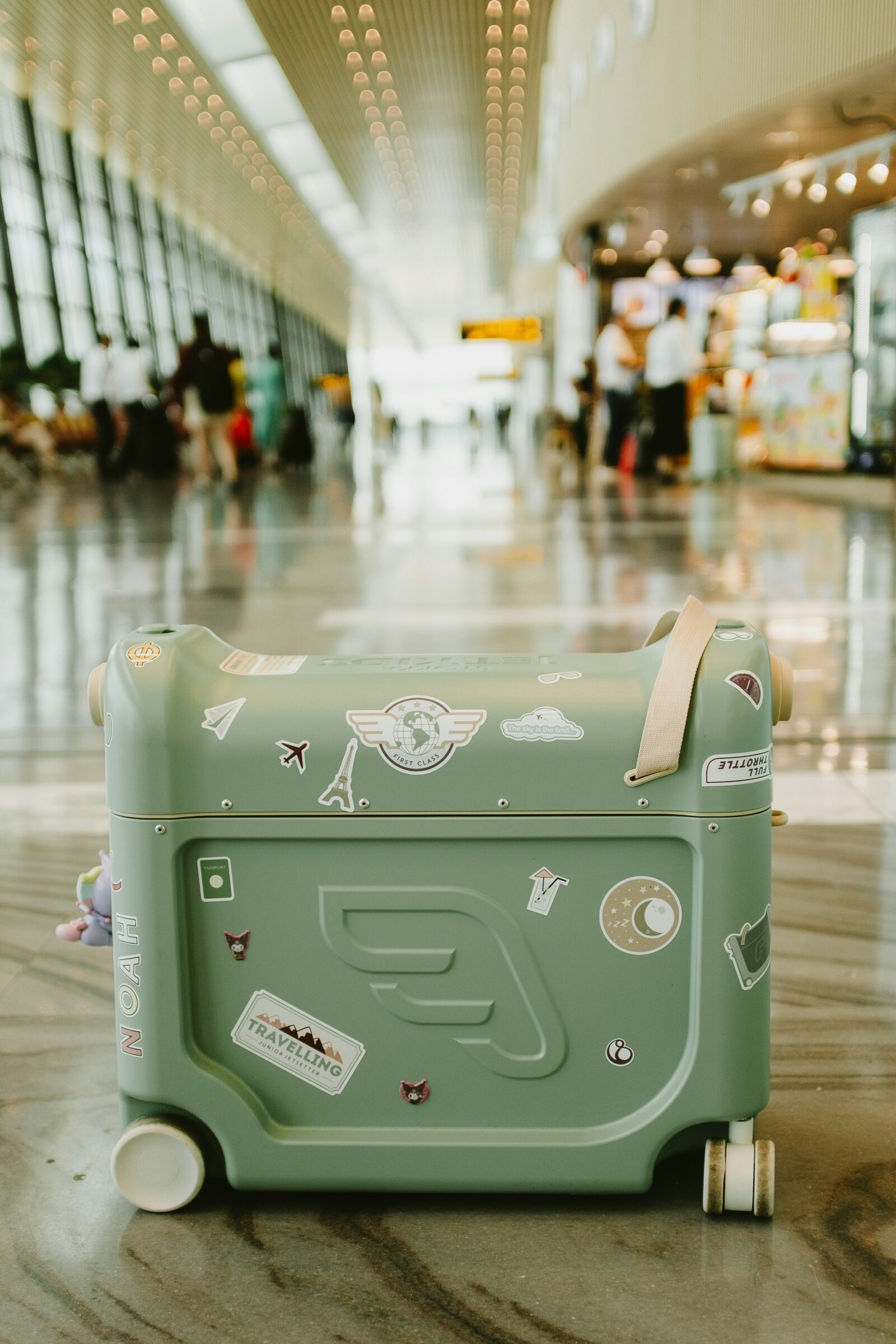 Green suitcase in an airport terminal, used to illustrate the best way to carry cash when flying—always keep it in your carry-on, not your checked luggage.