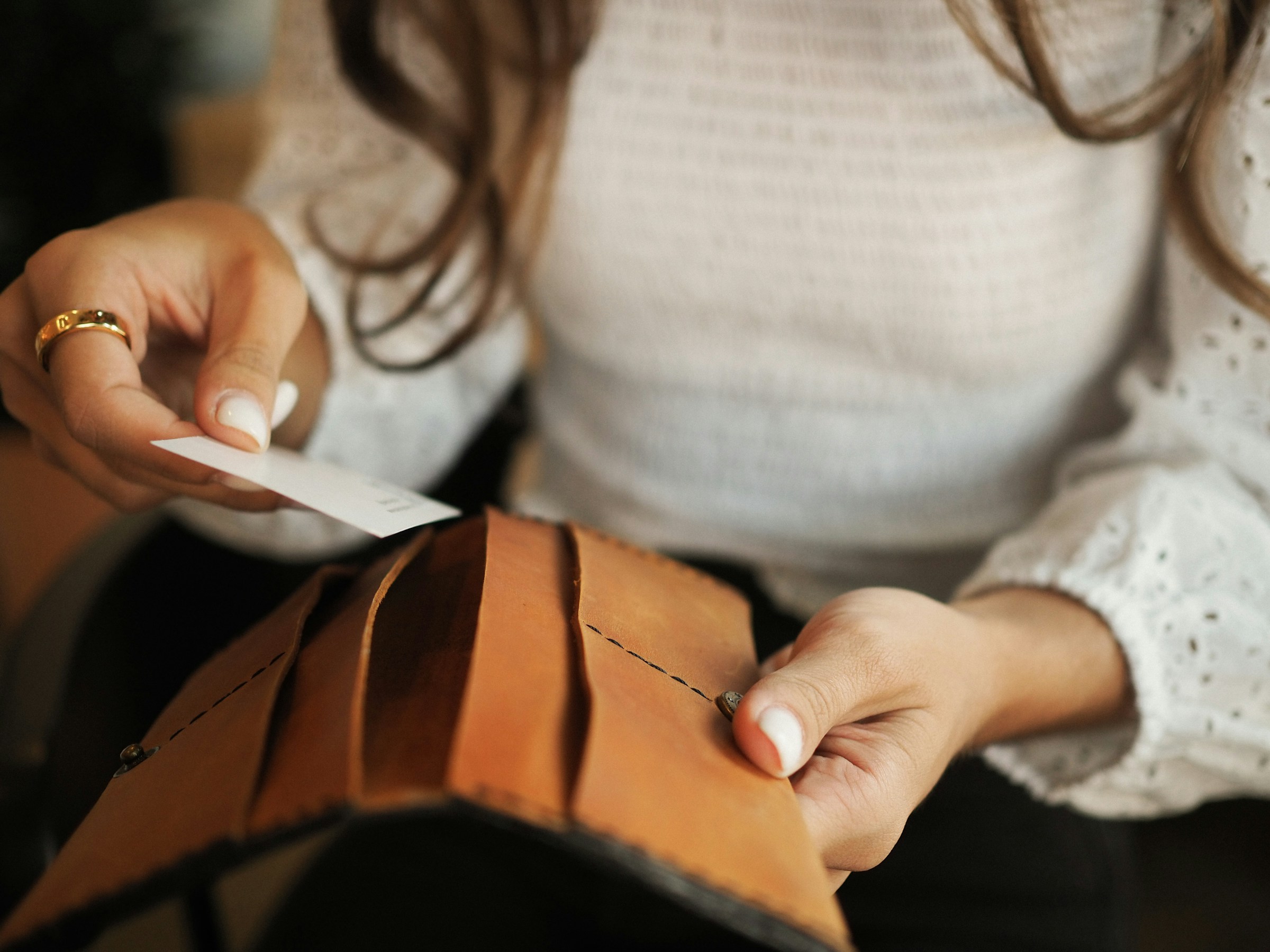 Woman opening a leather wallet and slipping in a card, showing a practical example of preparing a decoy wallet as part of the safest way to carry money while travelling.