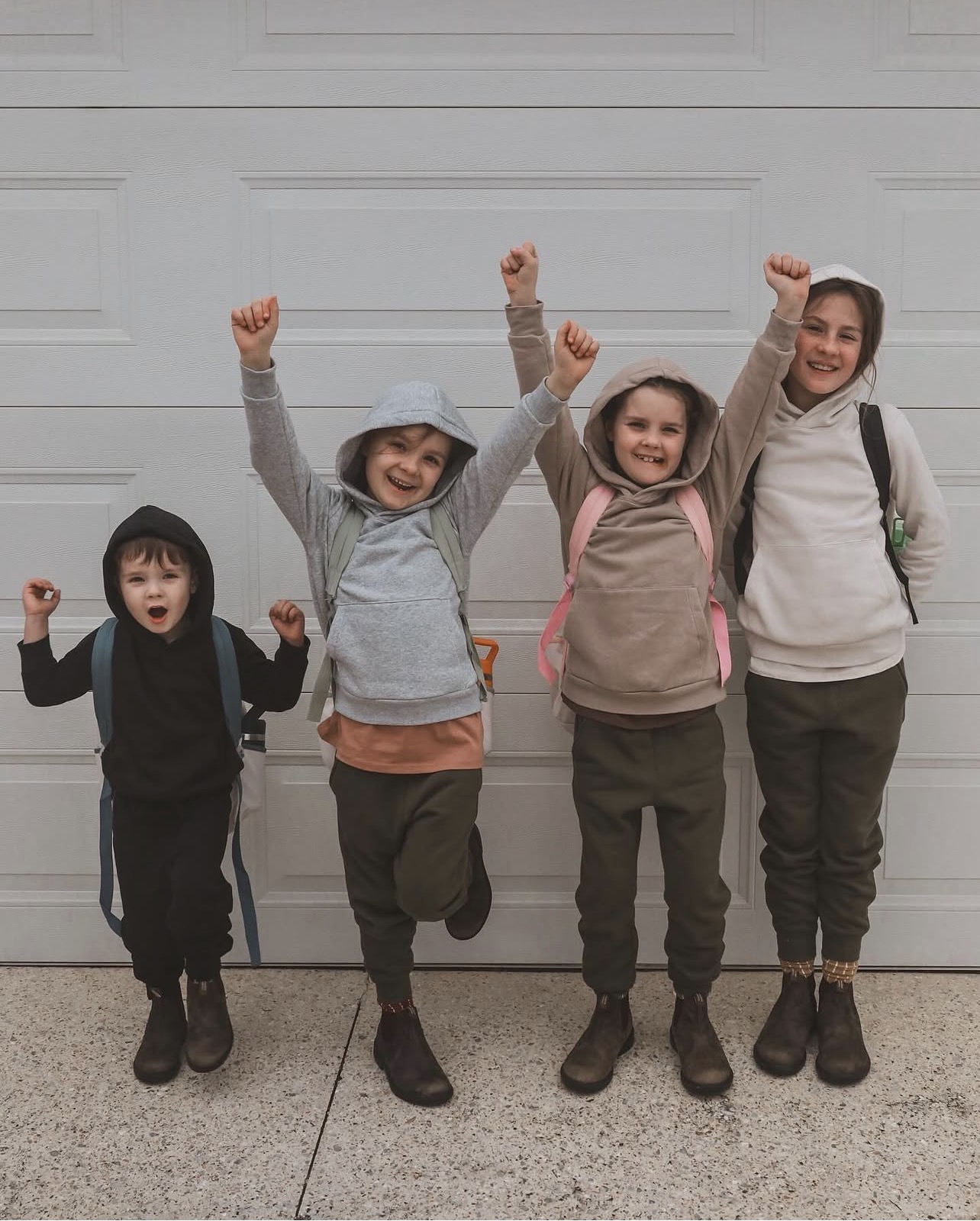 Four siblings, backpacks on and the youngest still toddler-sized, throw their fists in the air outside the garage, buzzing with pre-trip excitement.